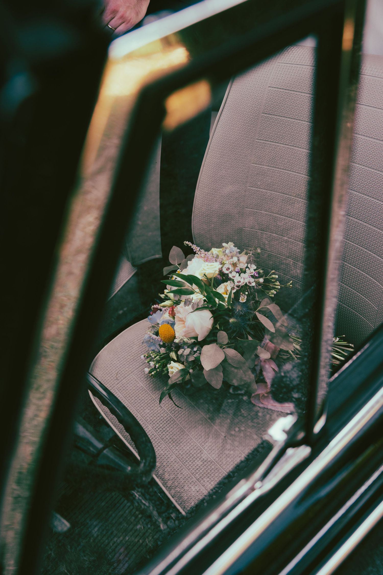 A delicate white and pink floral bouquet rests on a dark car seat.
