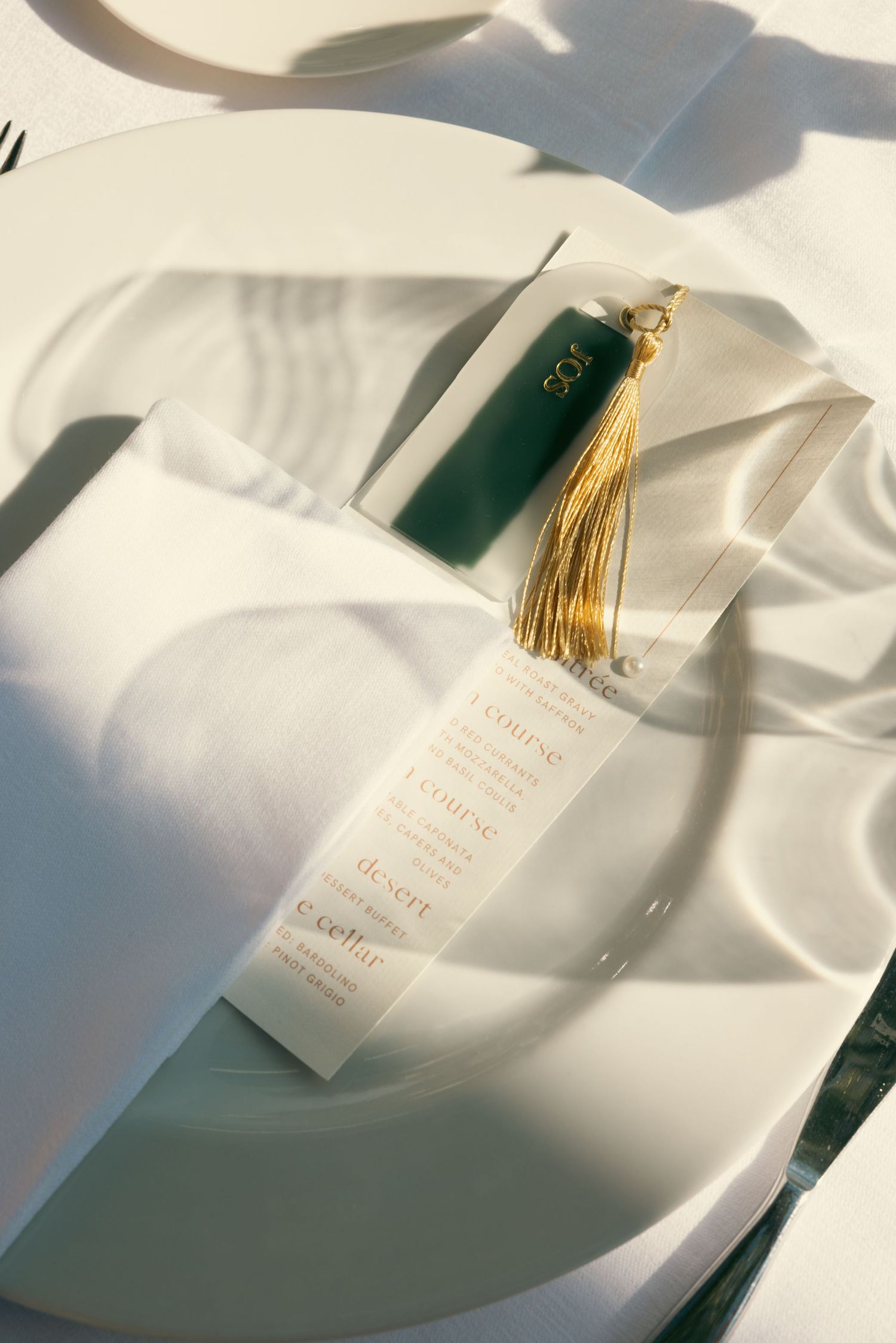 White graduation diploma with gold tassel photographed in soft natural light against white silk fabric background.