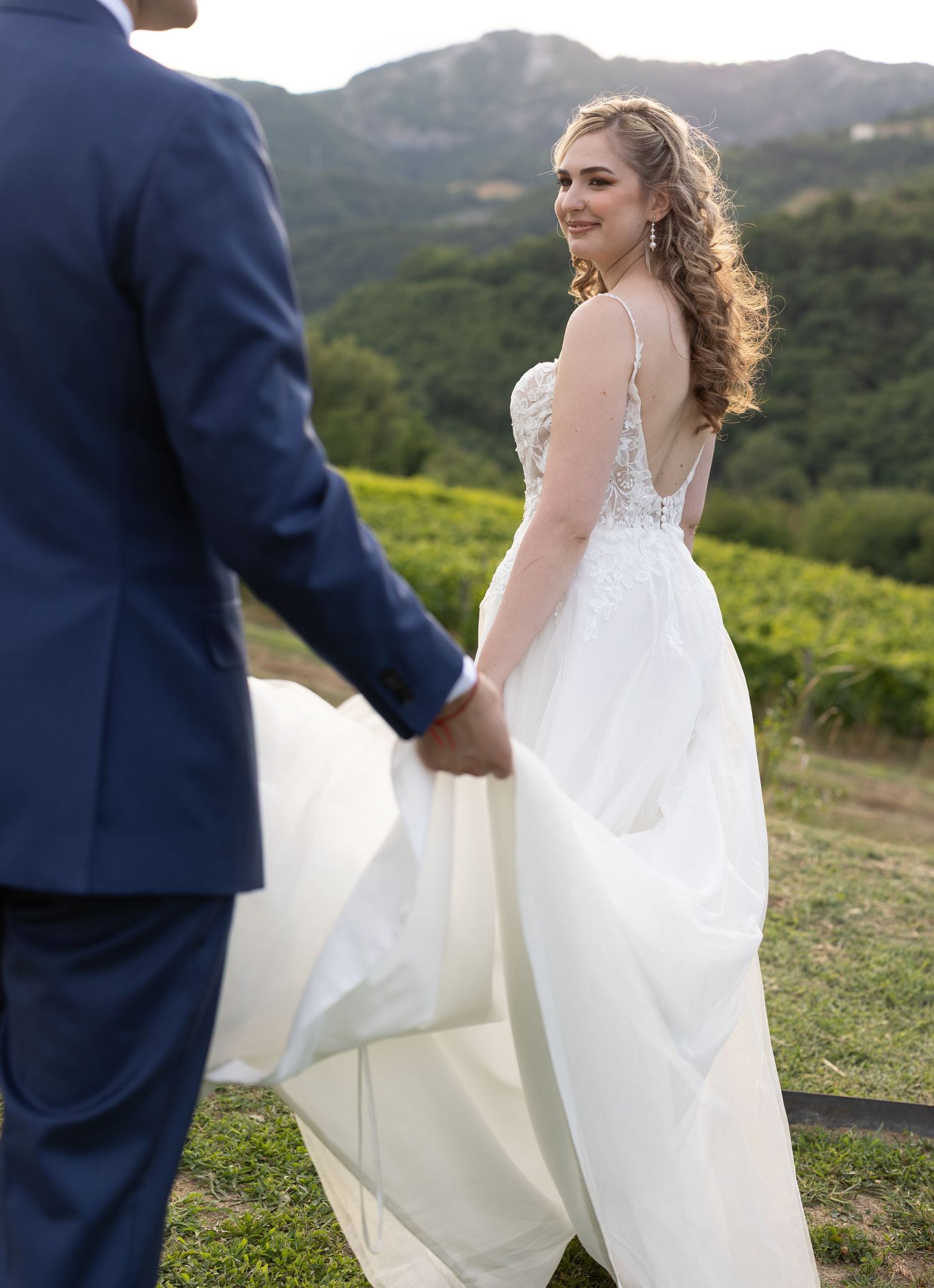 Bride in flowing white dress twirls against scenic mountain backdrop.