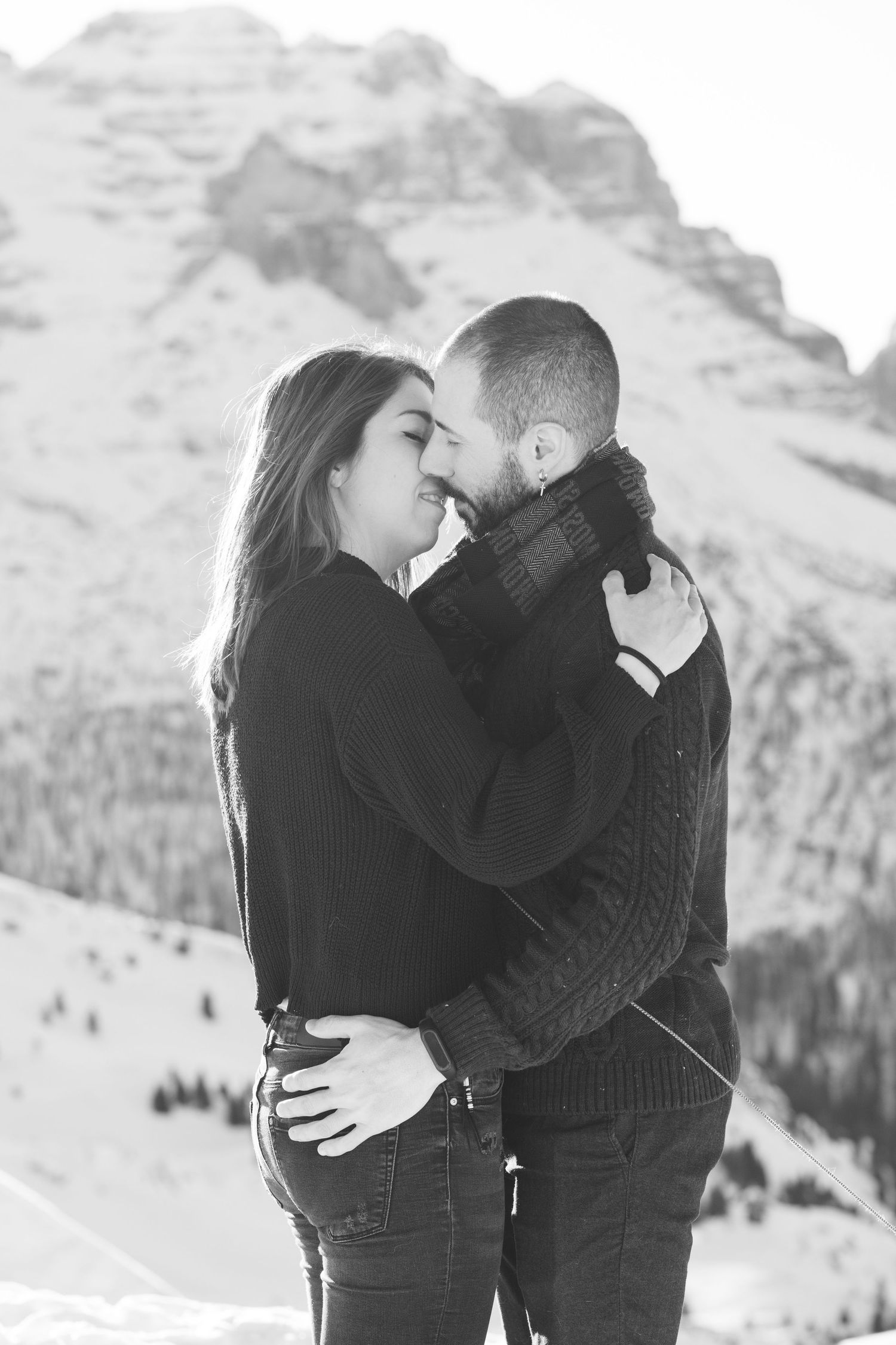 Winter engagement photos with snowy mountain backdrop showing intimate couple poses.