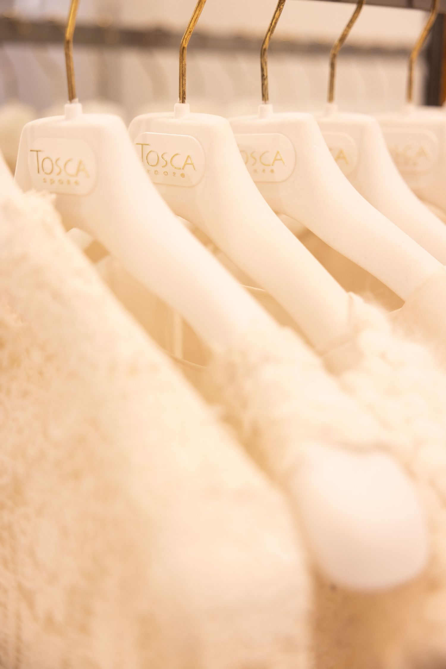 Row of white wedding dresses hanging on gold hangers in a bridal boutique.