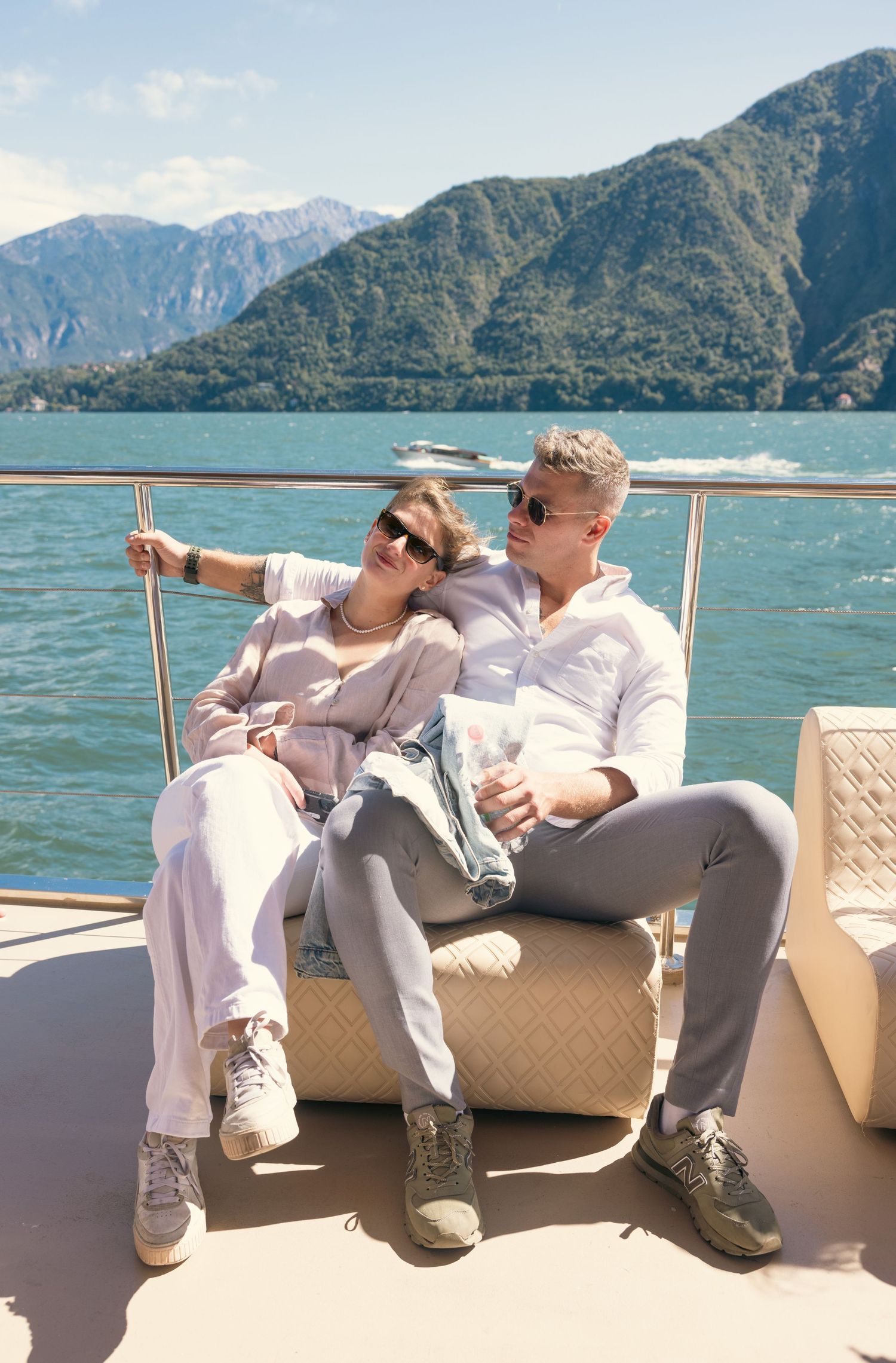 Couple relaxes on boat deck with stunning mountain lake views in background.