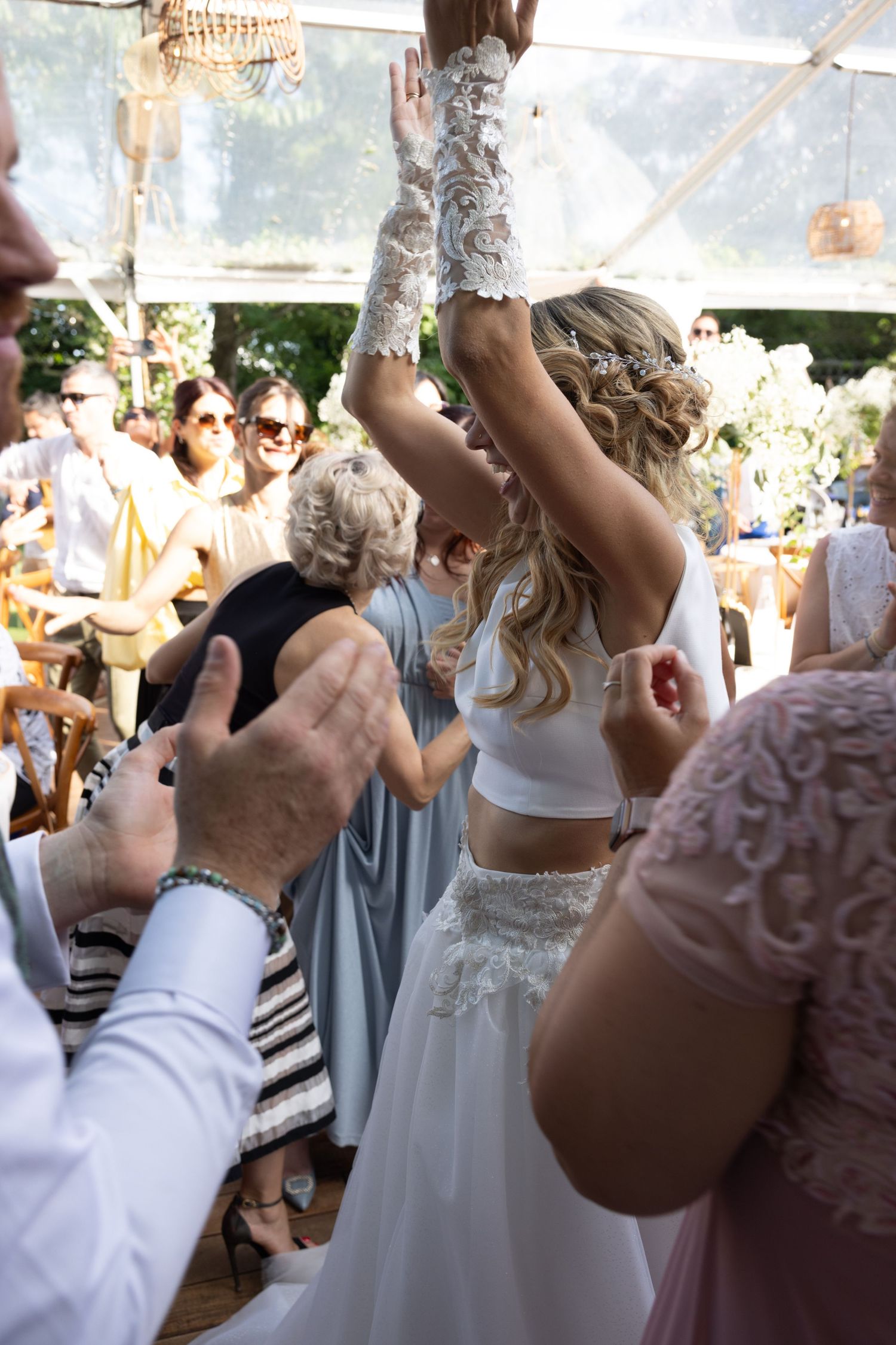 Wedding party celebrates with raised arms under an outdoor tent.