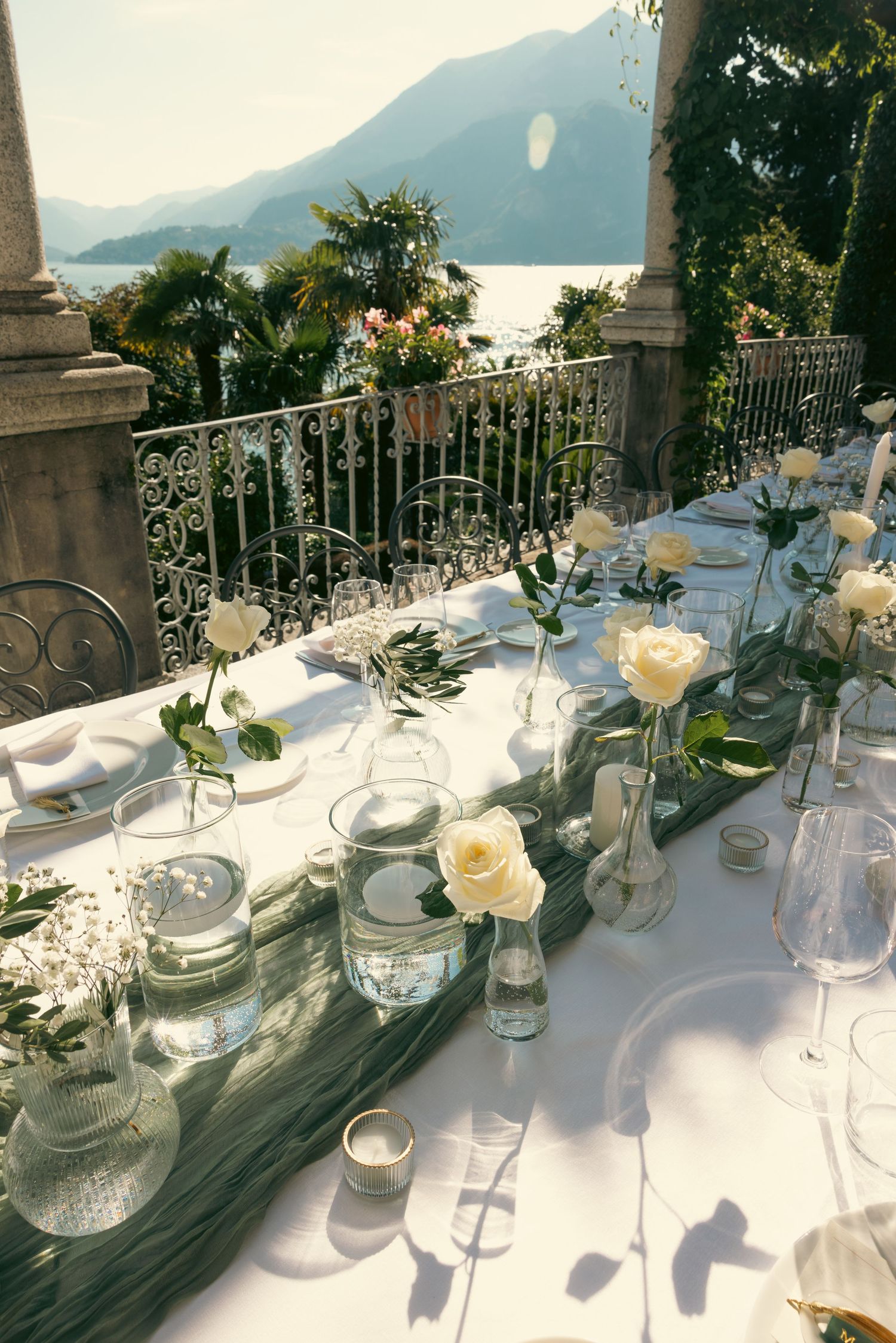 Elegant outdoor wedding table setting with white roses and glassware overlooking a scenic mountain landscape.