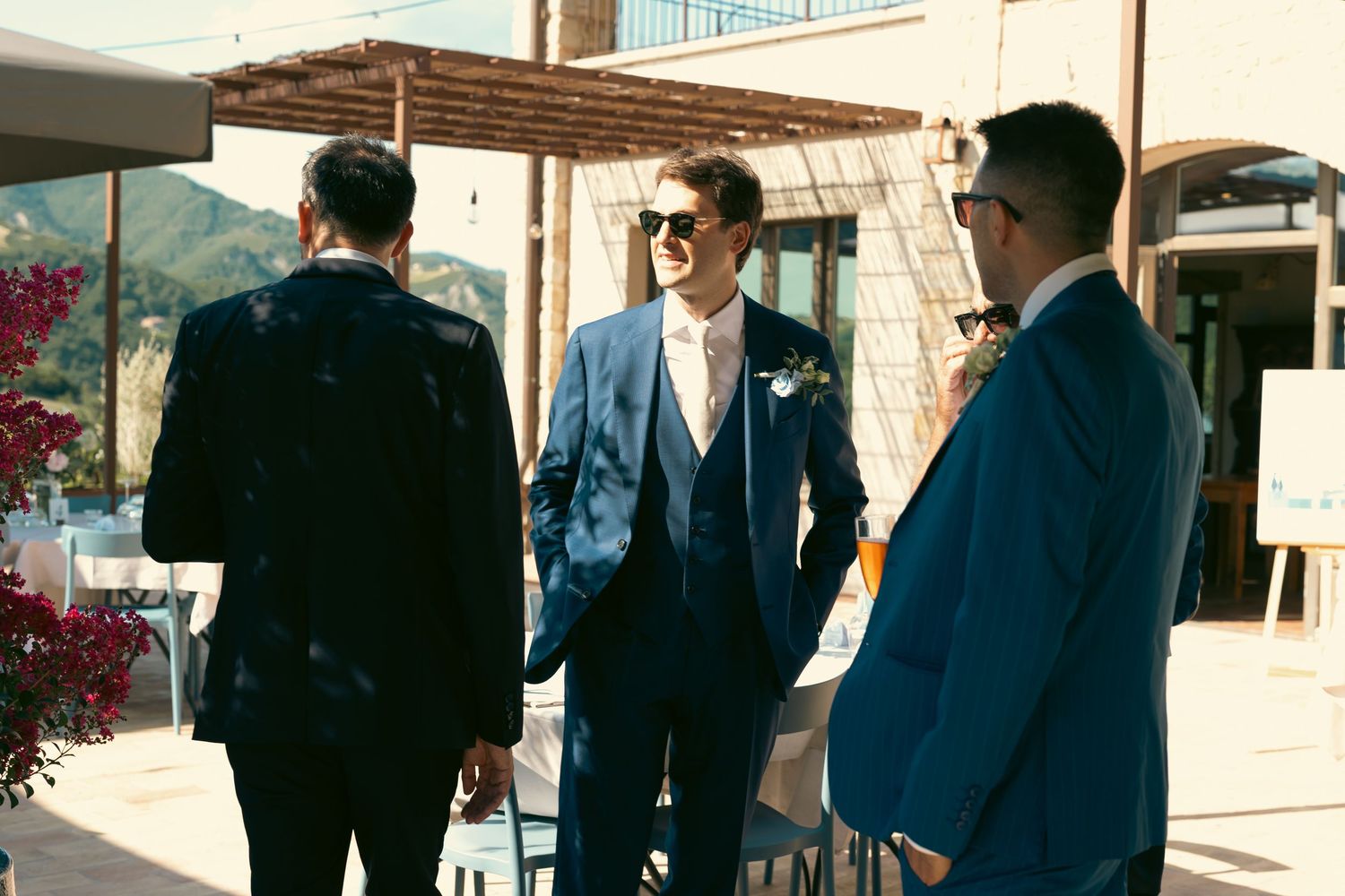 Group of groomsmen in navy blue suits standing outside a building.