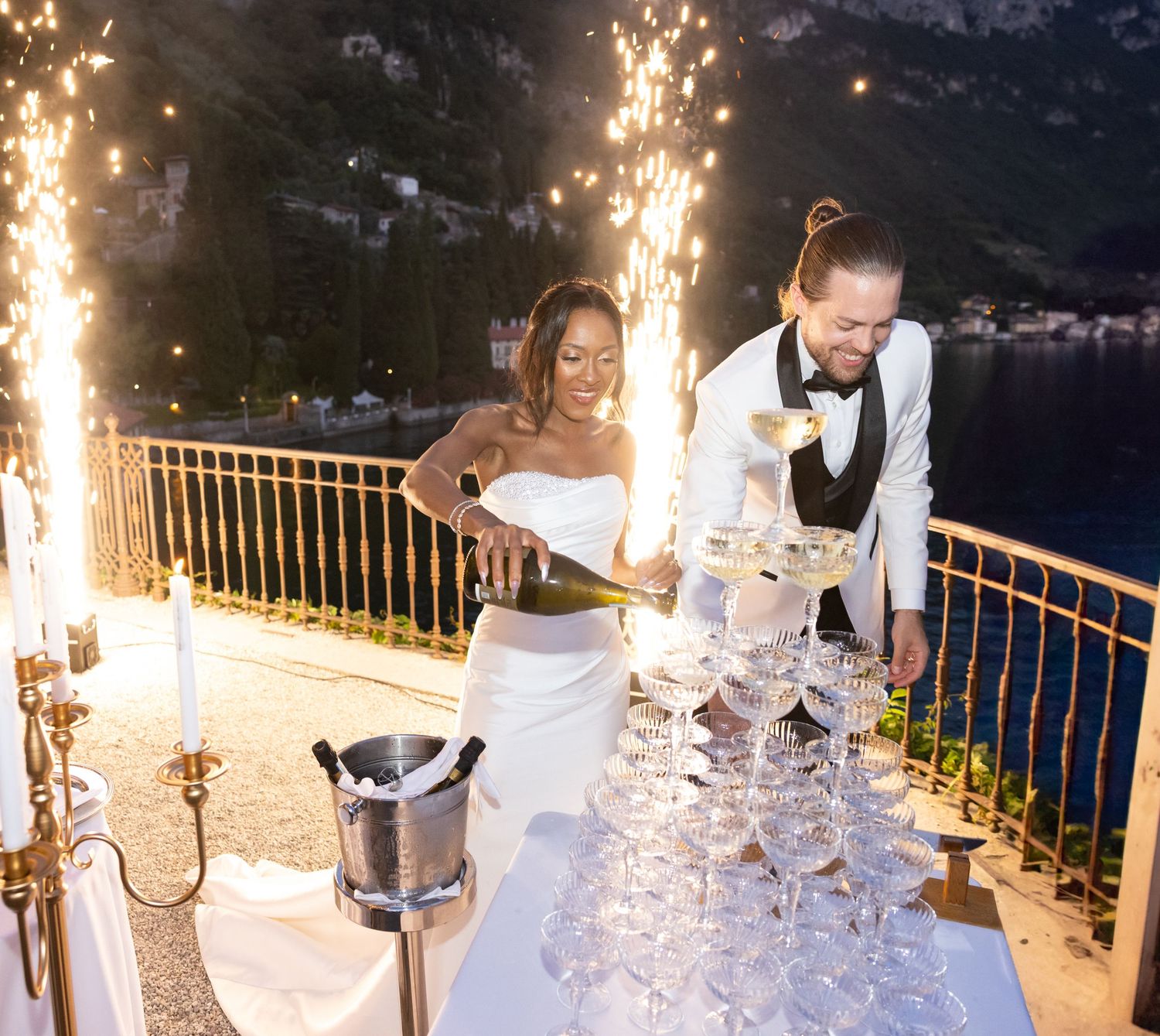 Champagne tower being poured with sparklers creating a dramatic nighttime display at an elegant outdoor event.