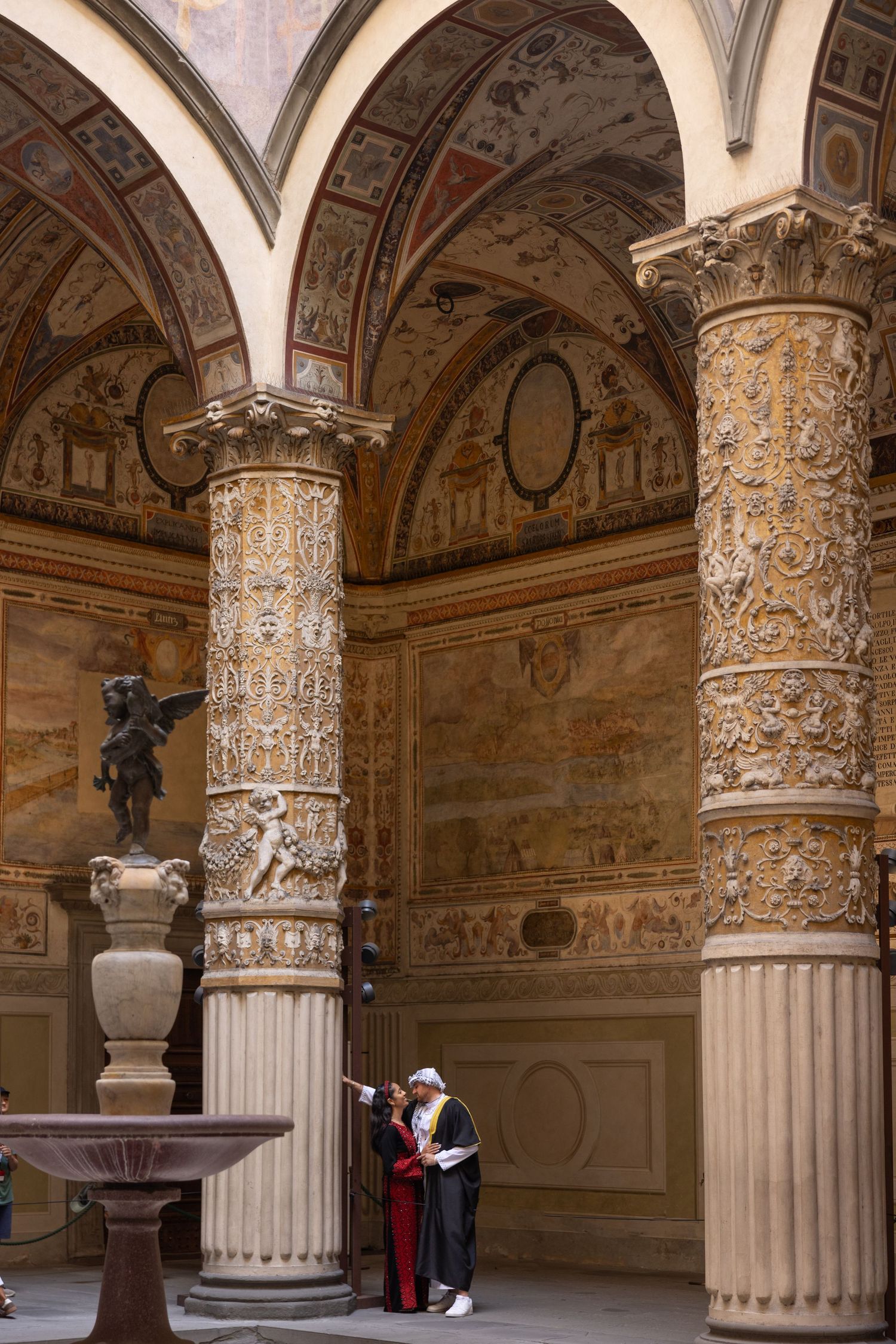 Ornate Renaissance columns with decorative capitals line a vaulted corridor in the Palazzo Vecchio of Florence.