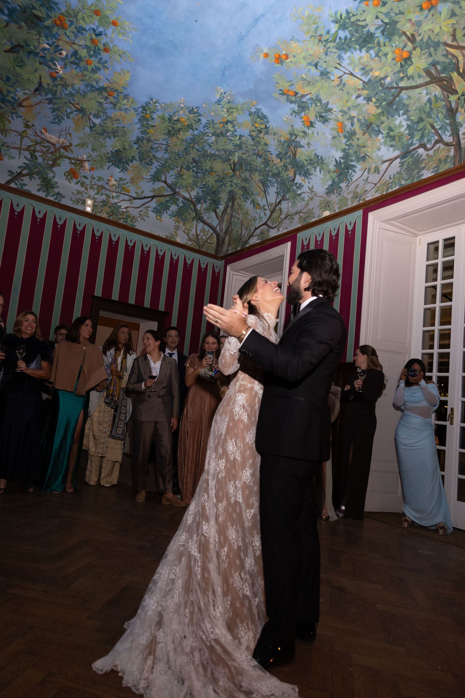 A couple performs a romantic dance together during their wedding reception under a painted ceiling with floral details.