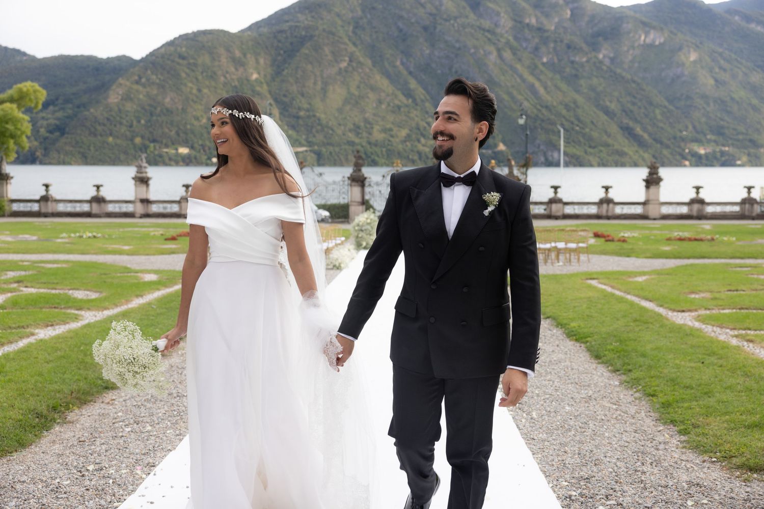 A couple in wedding attire walks along a scenic mountain path surrounded by natural landscape.