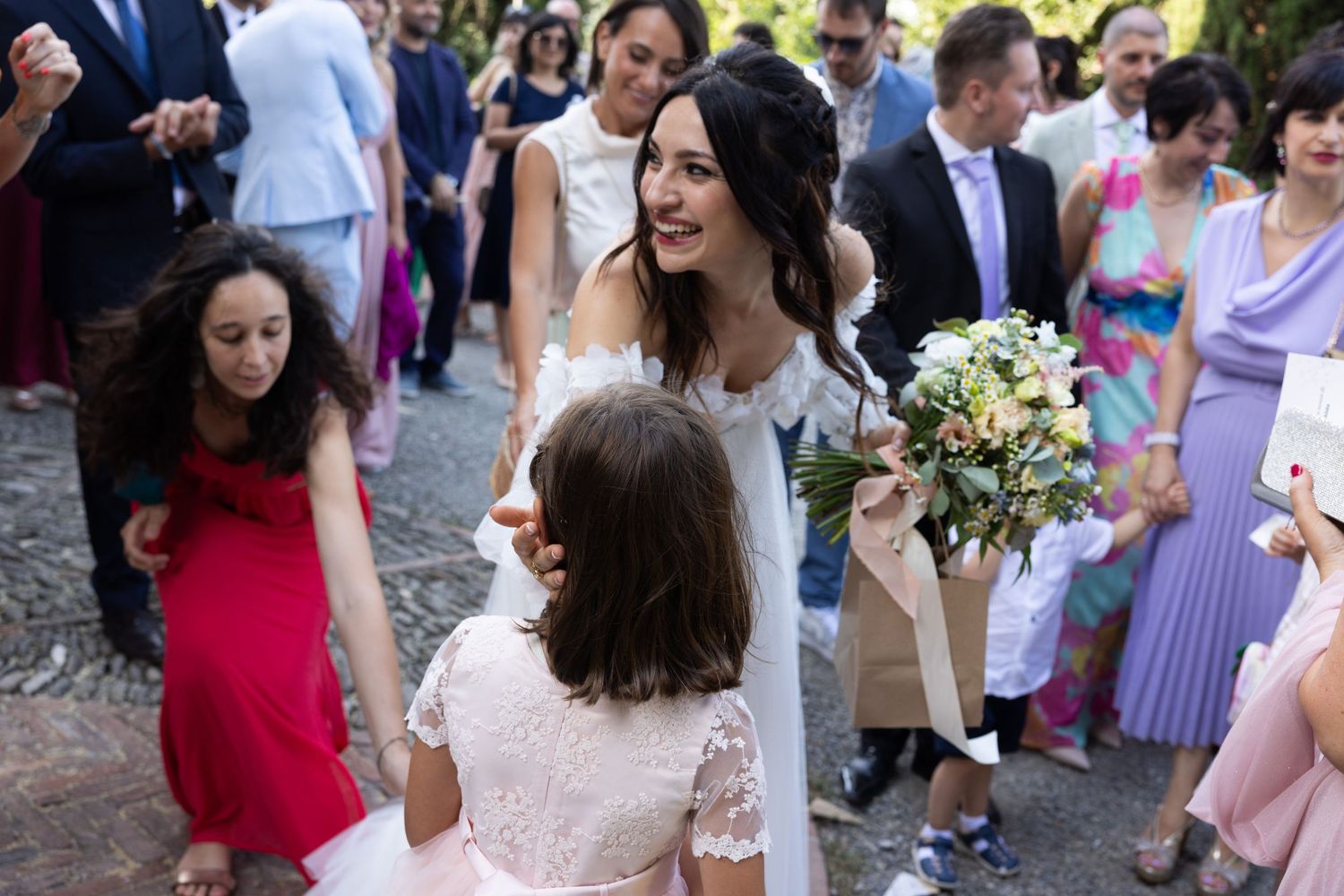 Wedding guests in colorful attire gather outdoors during a summer celebration.
