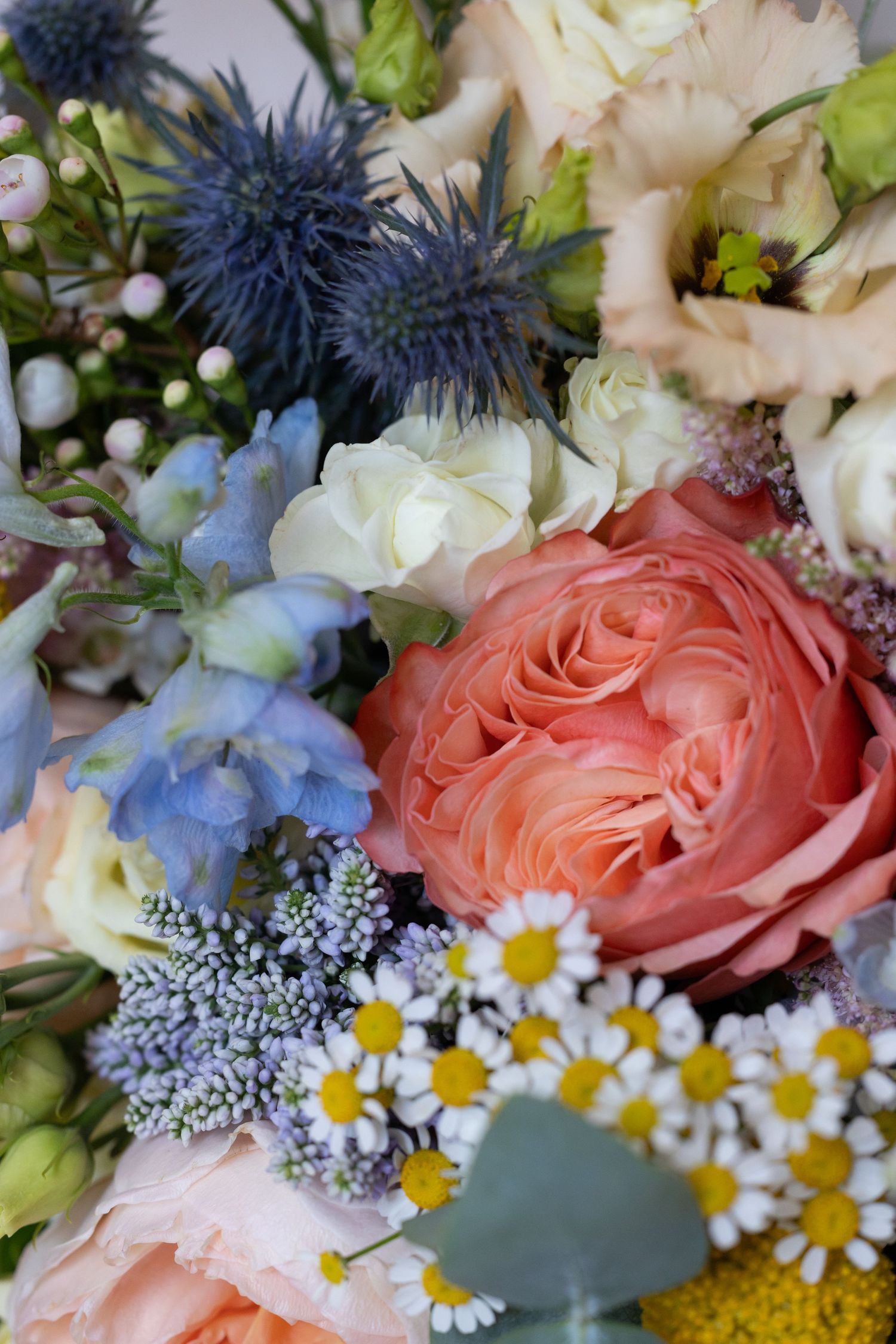 Wedding bouquet featuring coral roses, blue thistles, daisies and mixed flowers.
