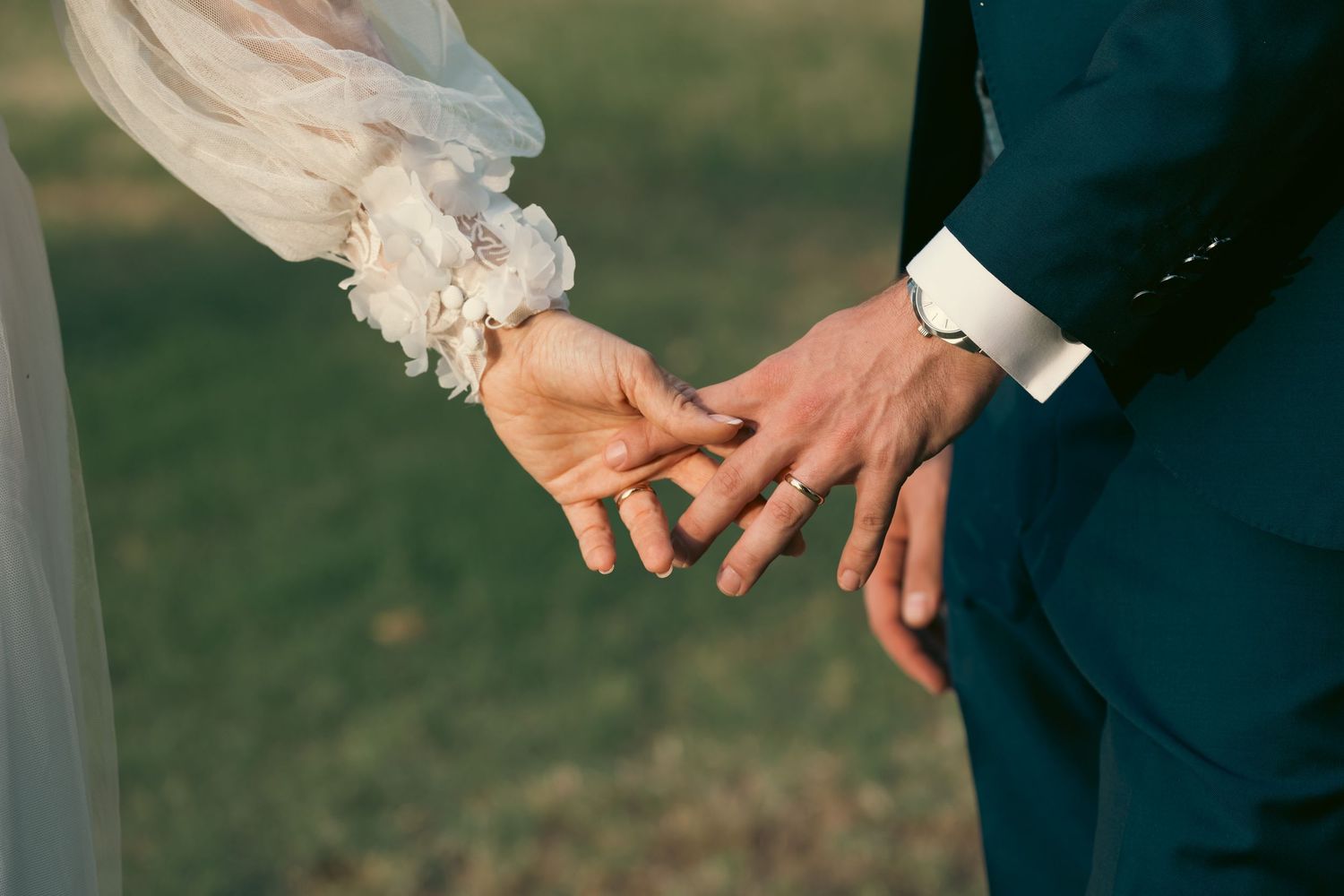 Close-up of hands and wedding dress details during outdoor ceremony.