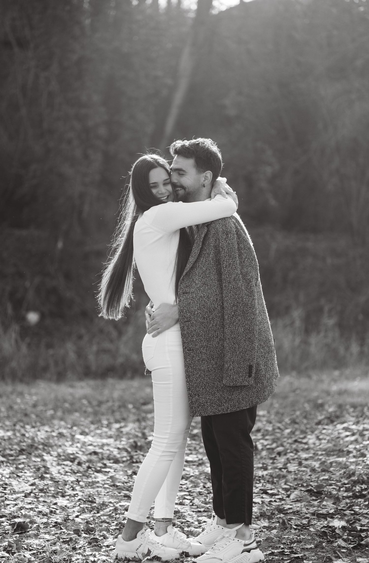 Couple embracing in a forest clearing with fallen autumn leaves scattered around them.