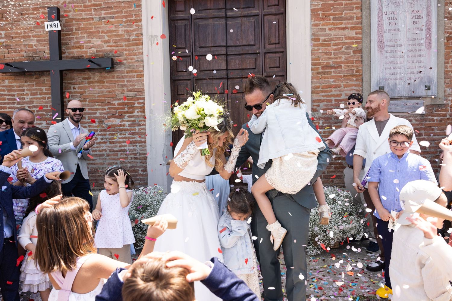 Guests celebrate outside brick church entrance during wedding confetti toss.