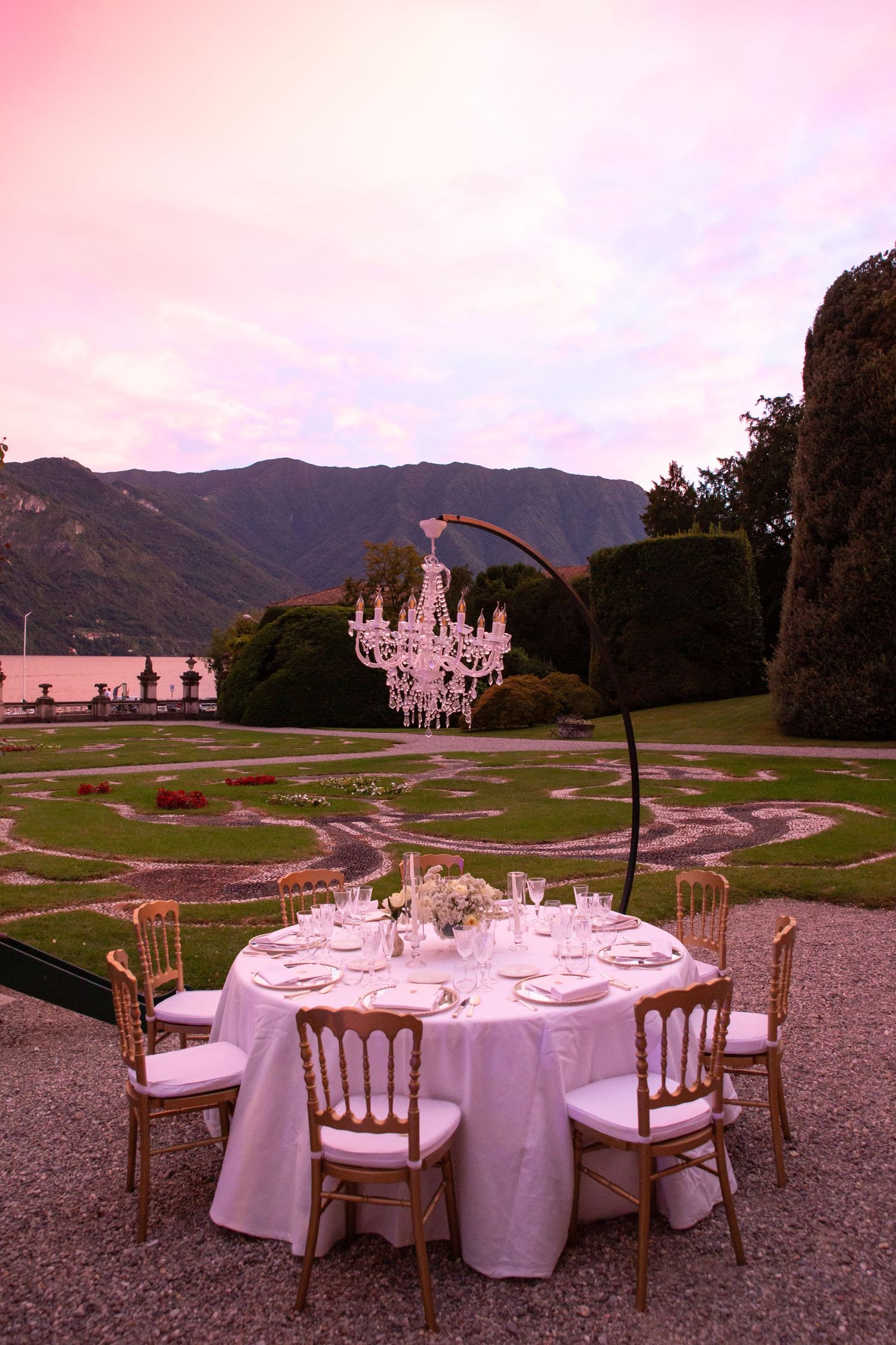 Outdoor wedding reception setup with round tables against mountain backdrop at sunset.