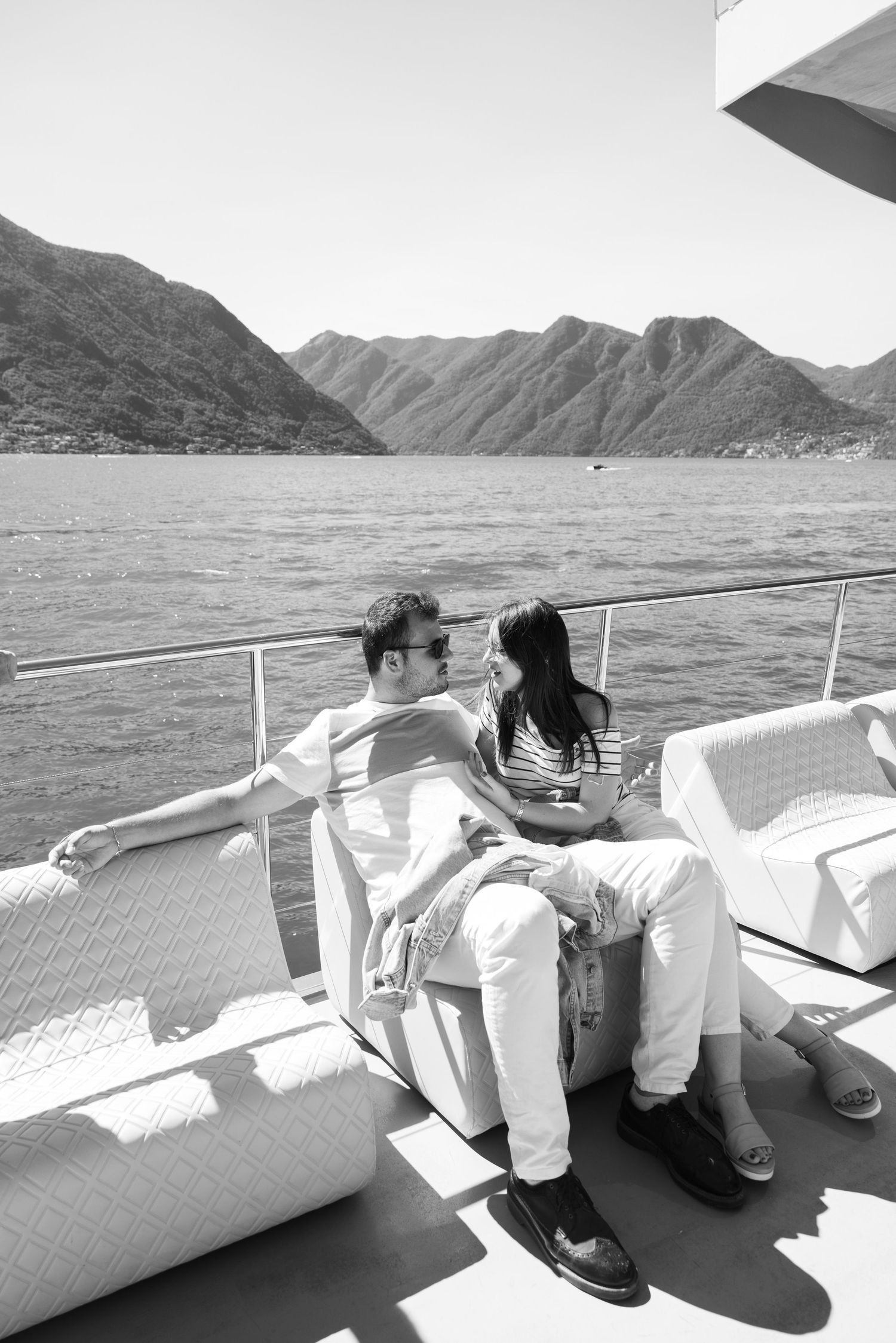 Black and white photo of people relaxing on boat seating with mountain views.