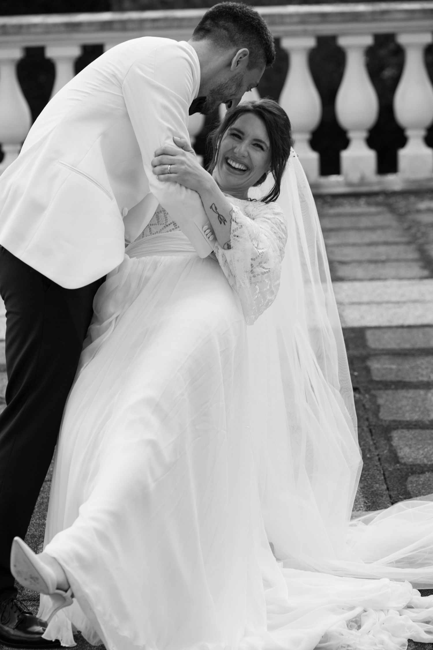 Black and white wedding photo capturing a joyful moment on stone steps with ornate railings.