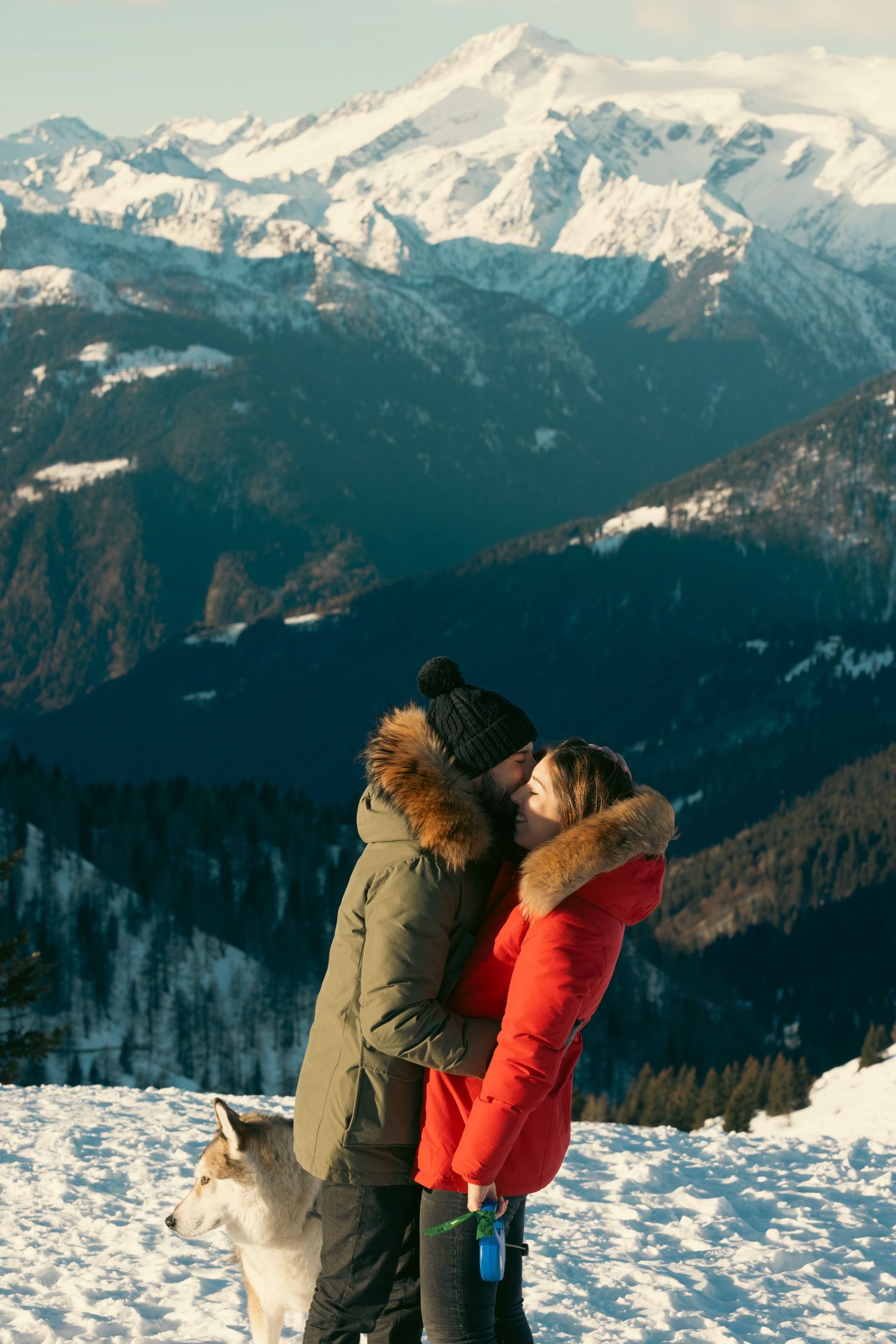 Two people in winter jackets admiring snowy mountain views from a scenic overlook.