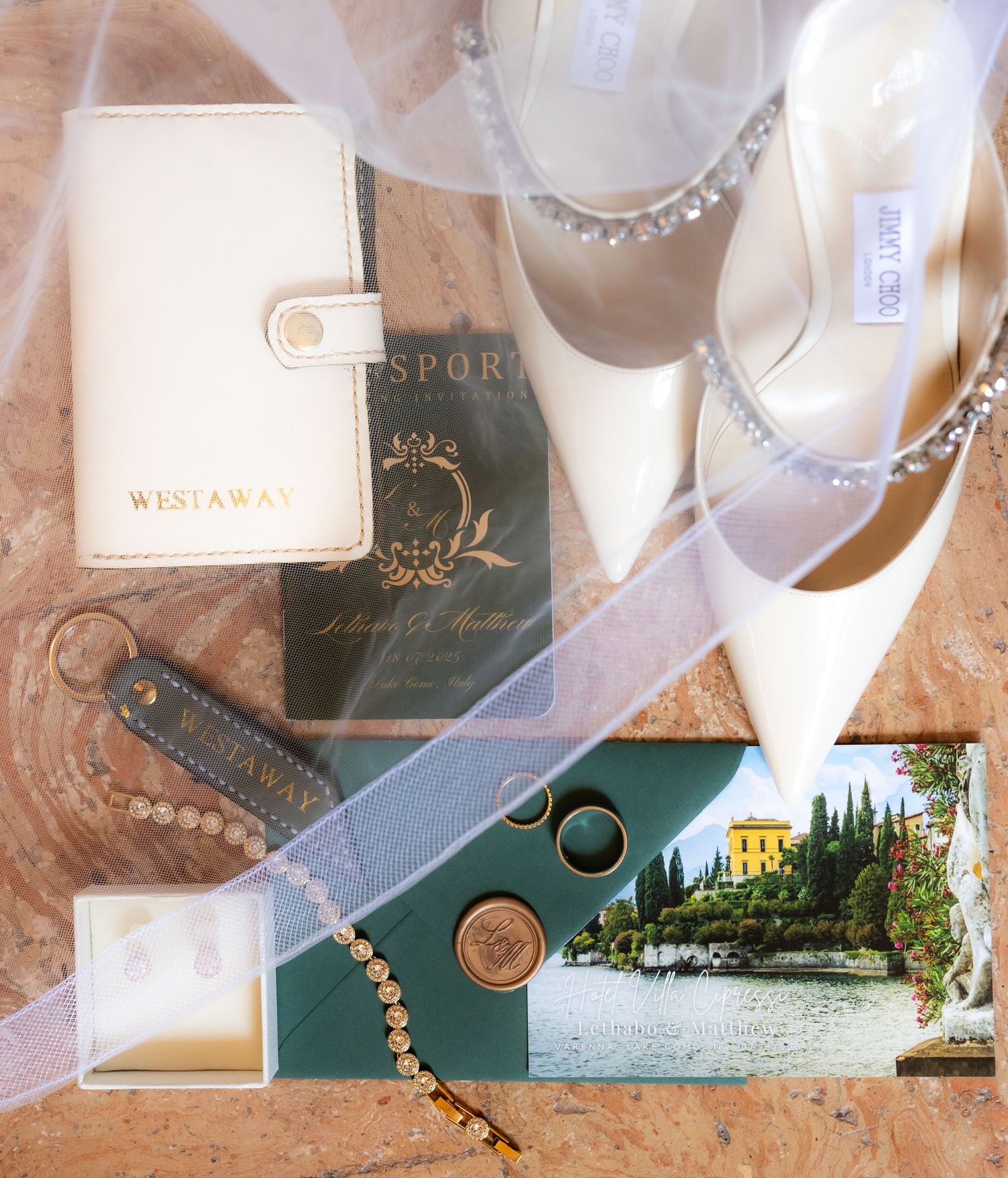 Wedding accessories including rings, pearls, and invitation cards arranged on a textured beige surface with soft lighting.