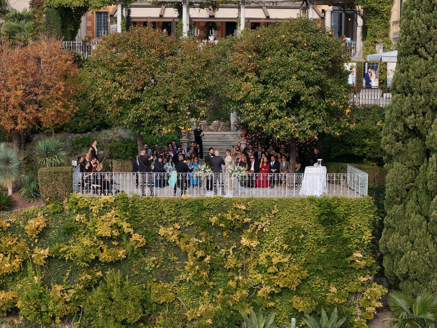 Autumn trees with yellow and orange foliage line a white railing fence along a walkway in a park setting.