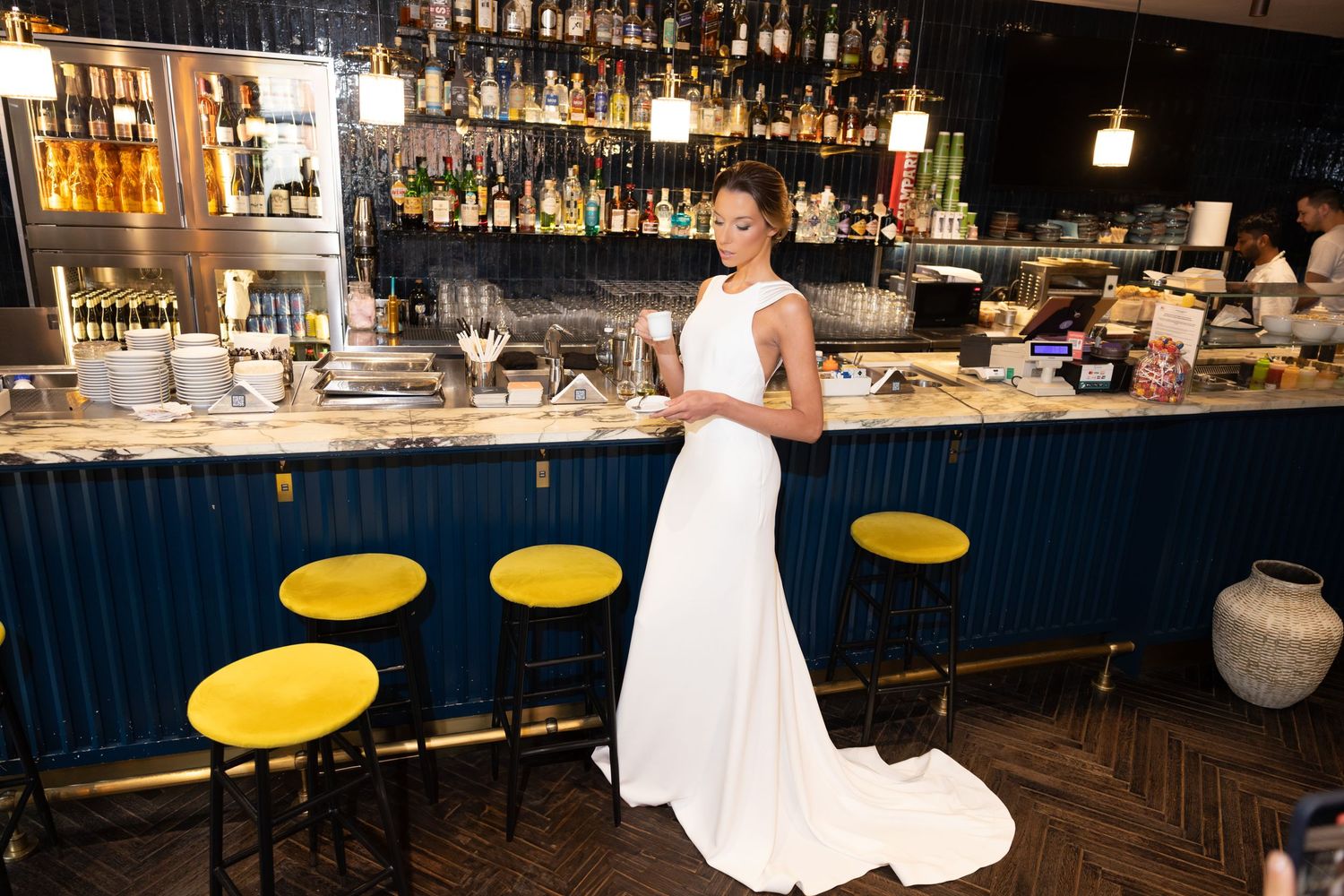 Modern bar interior with navy blue accents and yellow stools featuring a flowing white gown.
