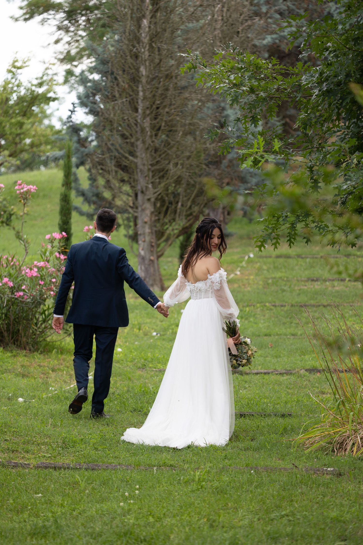 Couple walking through a garden path surrounded by trees and pink flowers.