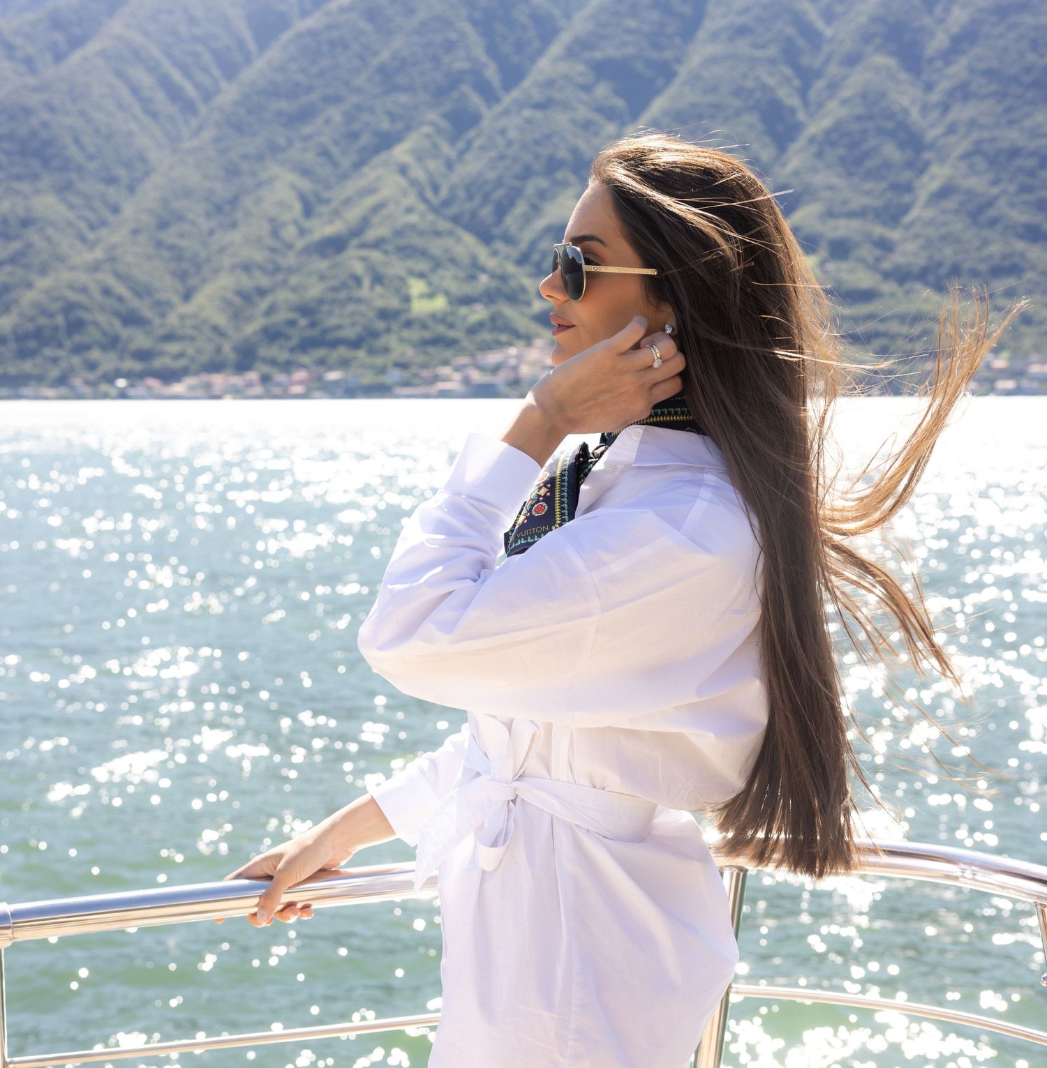 Woman in white outfit enjoying views from a boat deck on a bright day.