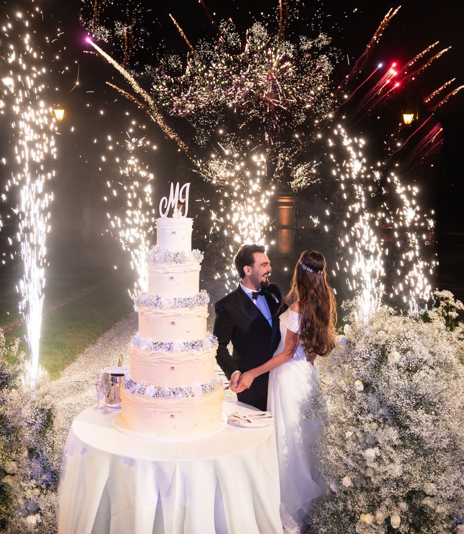 Elegant white wedding cake with dramatic sparkler display during evening reception.
