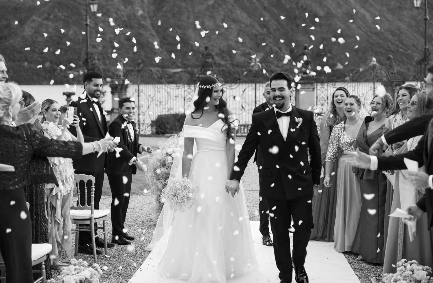 Black and white wedding photo with guests throwing confetti during outdoor celebration.