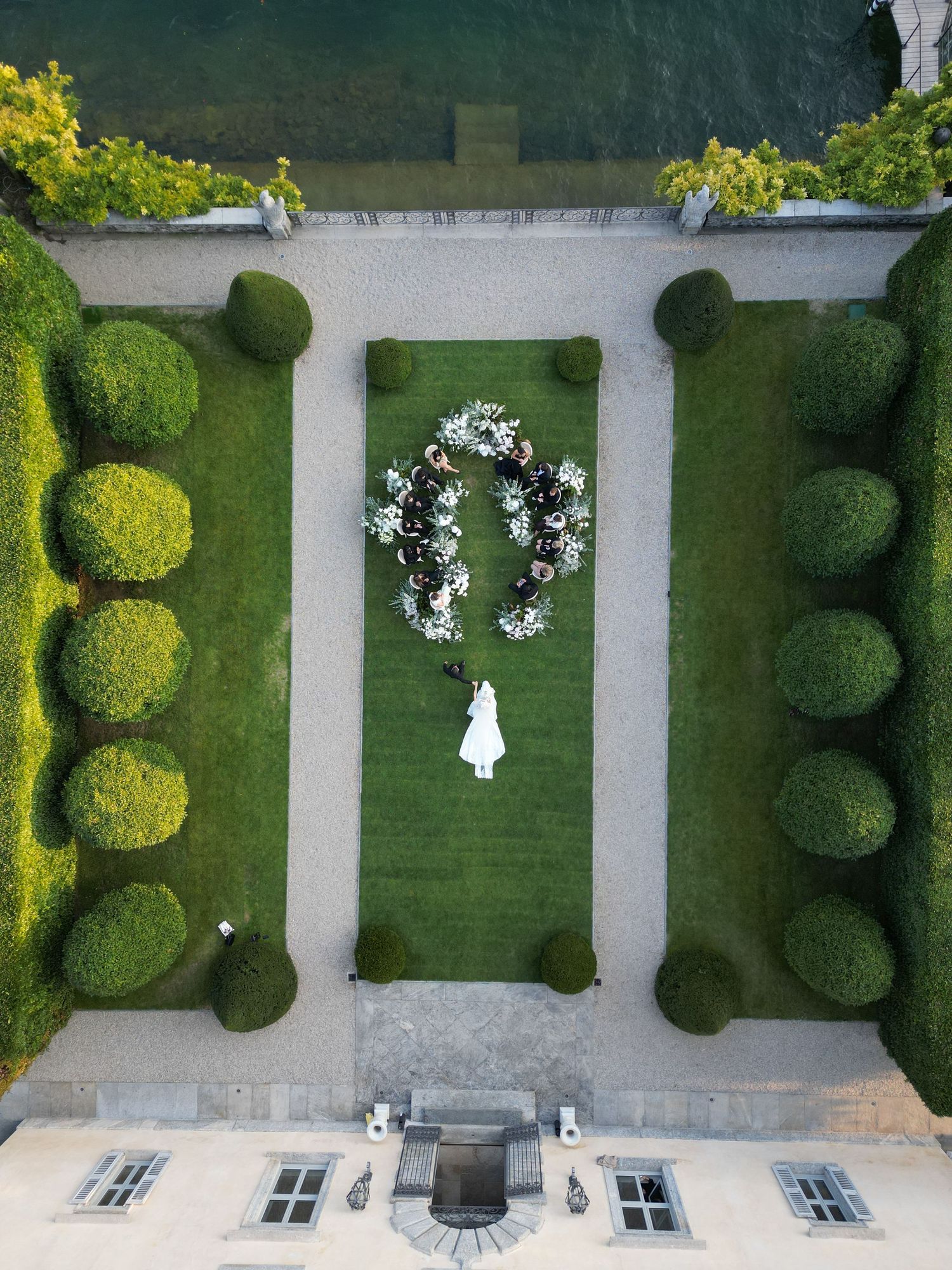 Aerial view of a symmetrical garden with manicured topiary bushes and white pathways forming a geometric pattern.