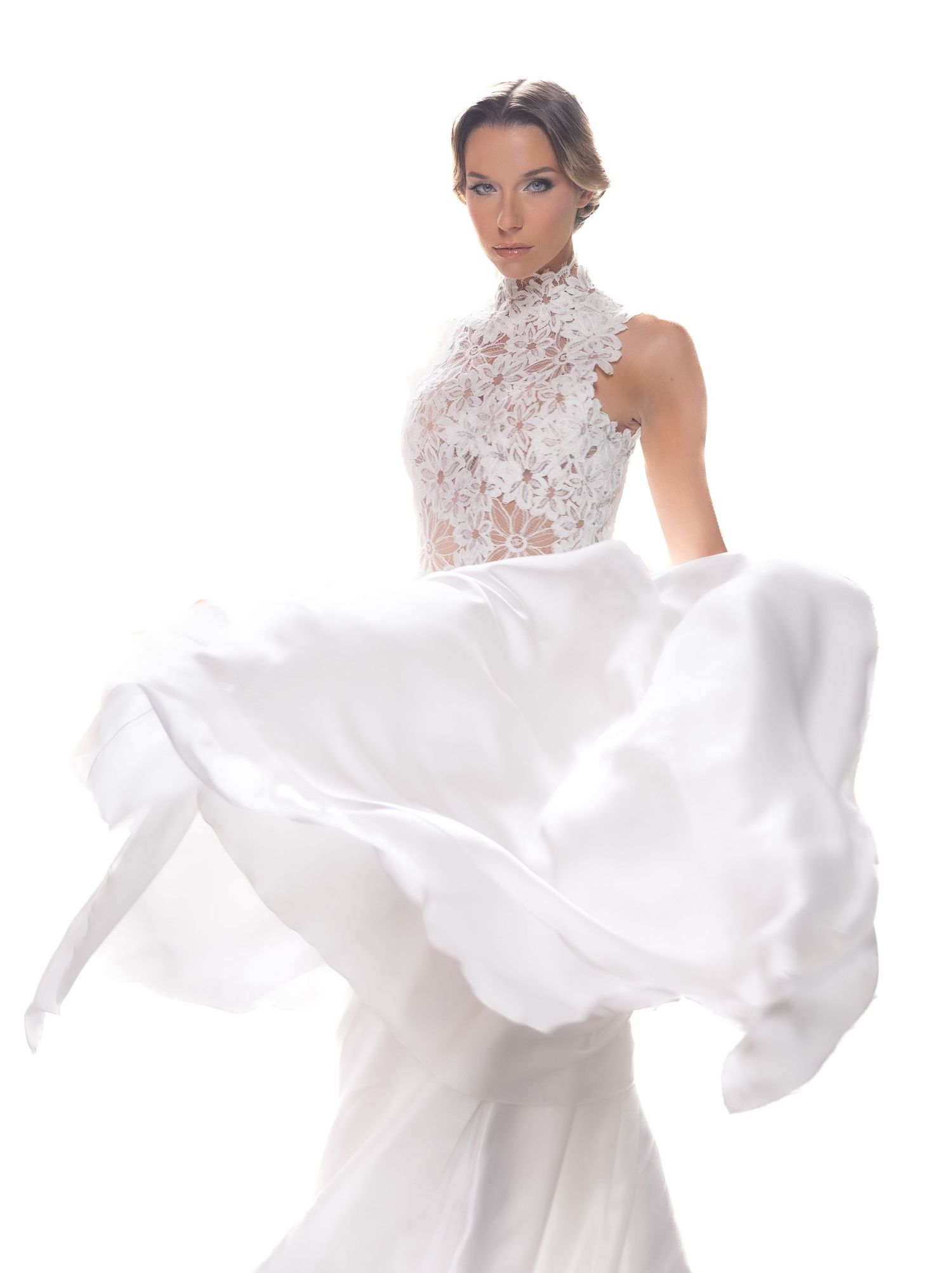 Flowing white wedding gown with lace details captured in dynamic motion against white background.