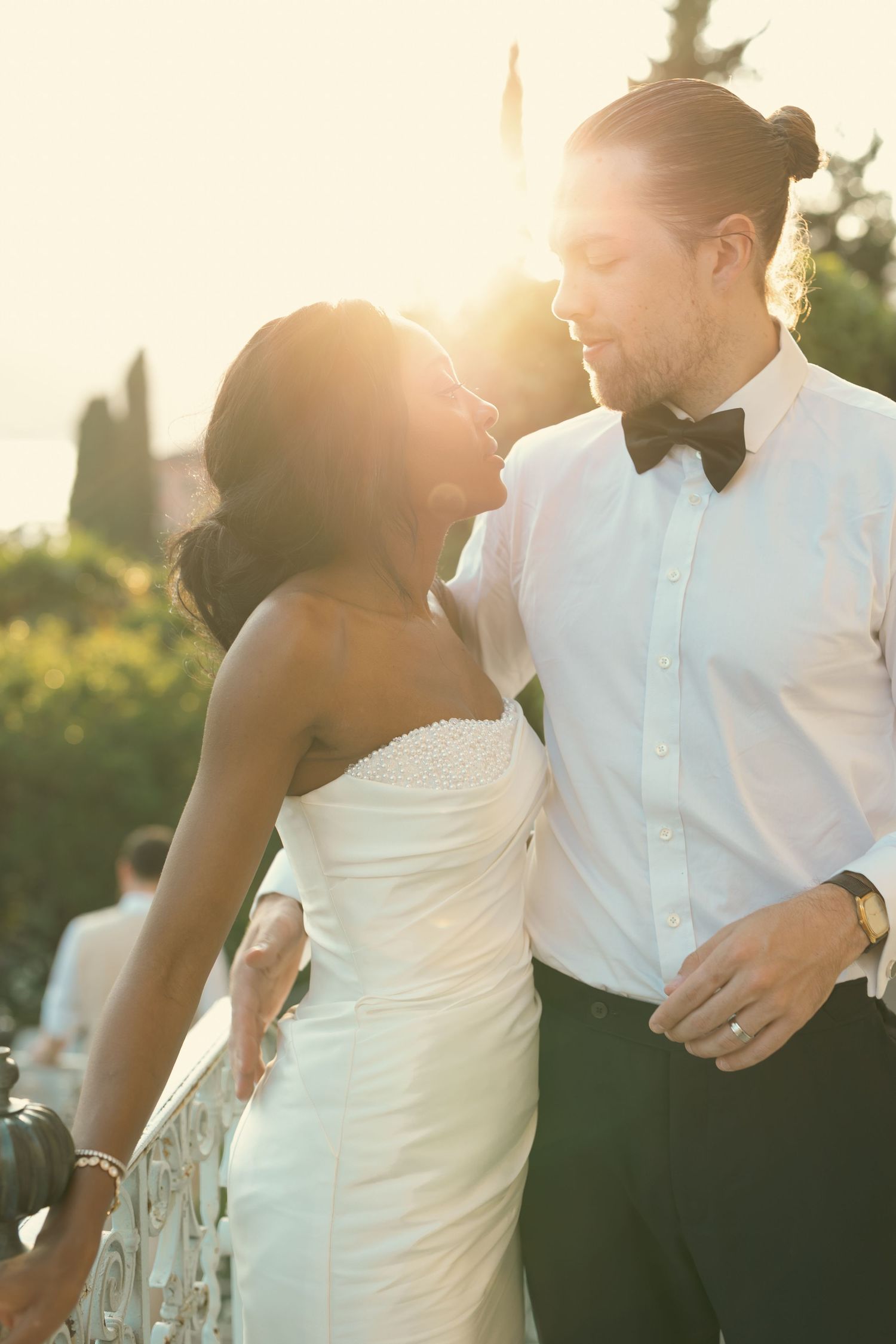 A romantic wedding couple embraces in golden sunlight during an outdoor sunset photoshoot.