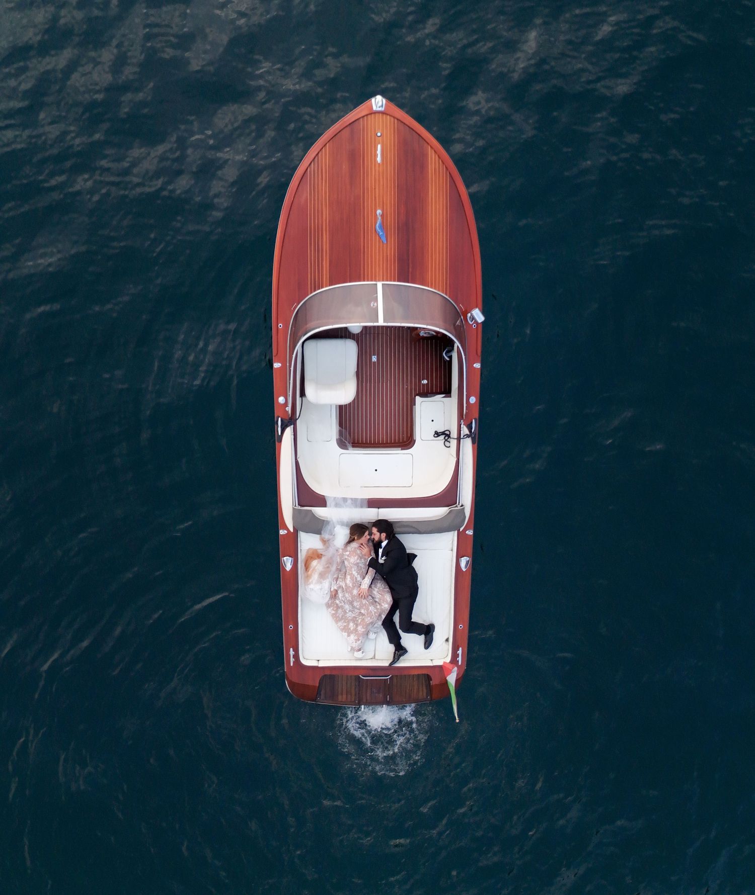 Aerial view of a vintage wooden Riva boat with rich mahogany deck cruising through dark blue waters.