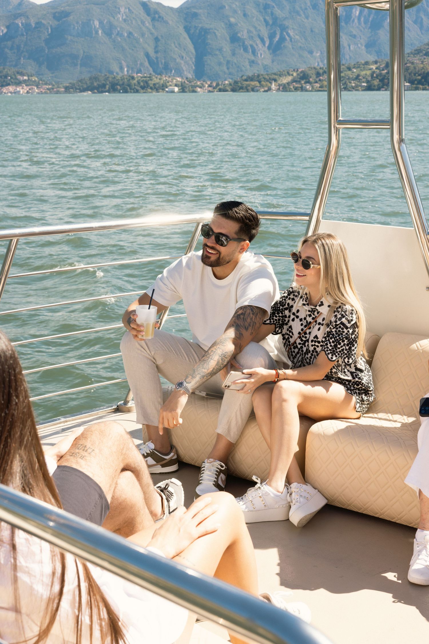 Group enjoying drinks and conversation on a yacht with scenic mountain backdrop.