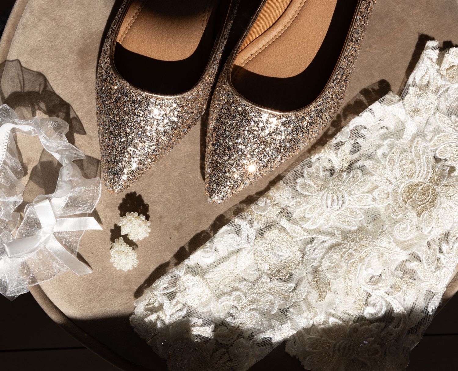 Sepia-toned close-up of sparkly bridal shoes with lace details.