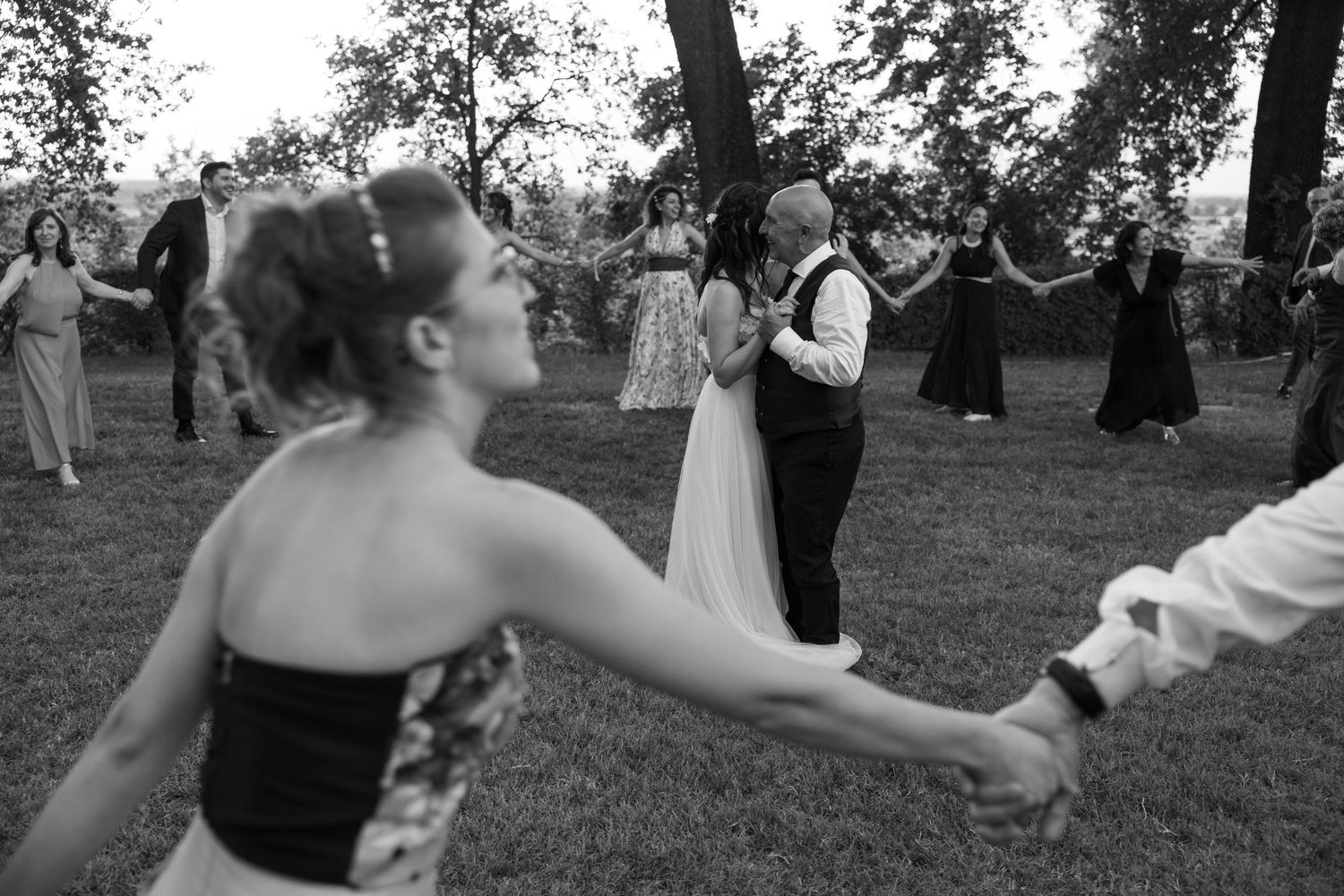 Wedding guests dancing and celebrating on a grassy lawn during daytime festivities.