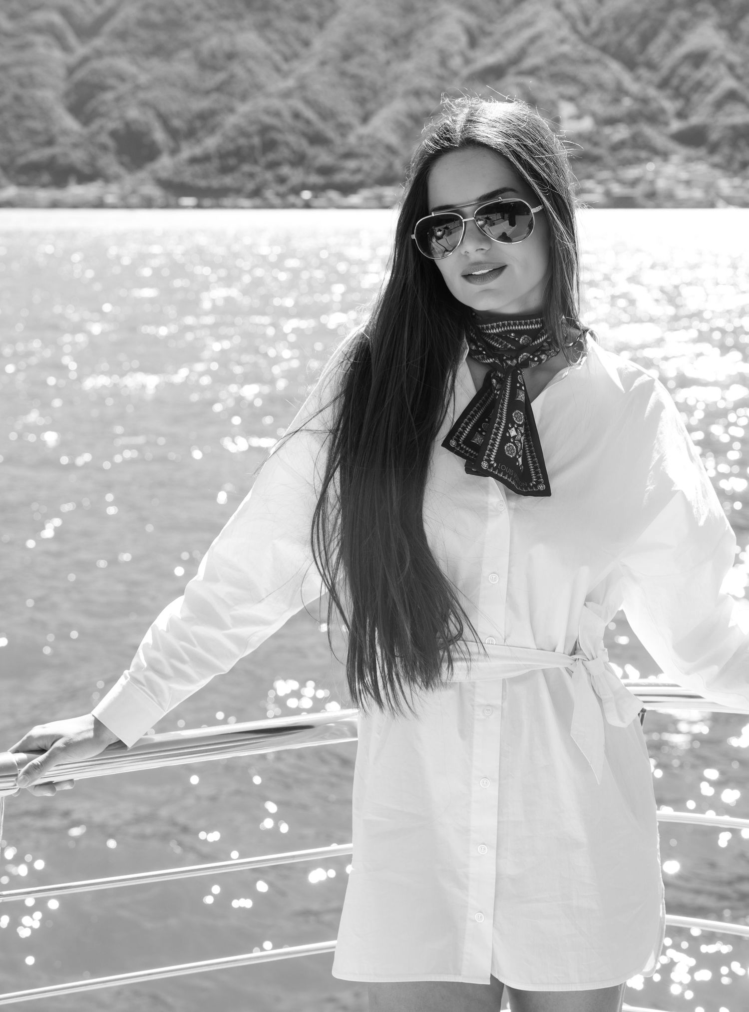 Woman in white blouse posing on a boat deck with sunlit water behind.