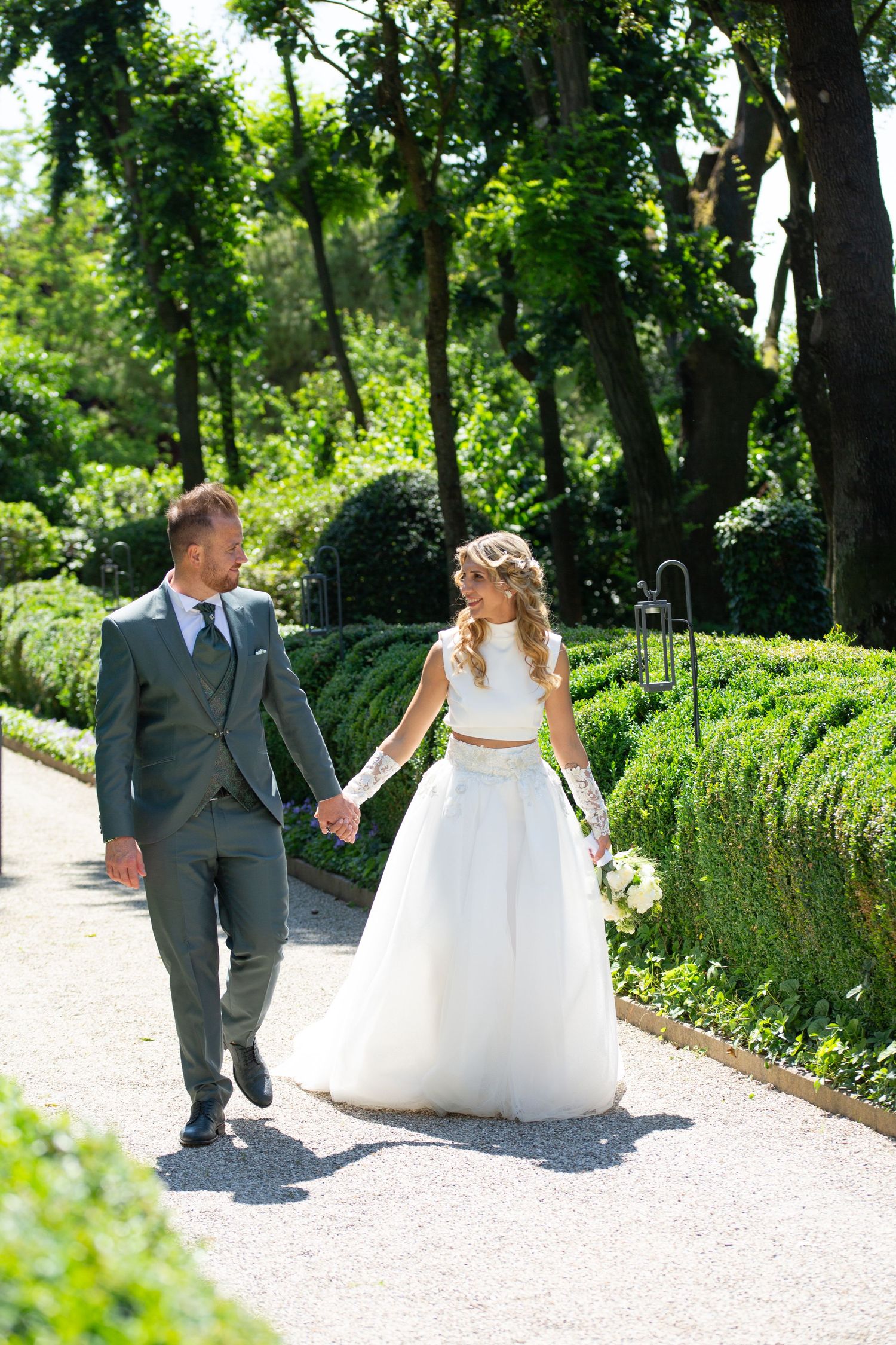 Couple walks along a garden path surrounded by lush greenery on their wedding day.
