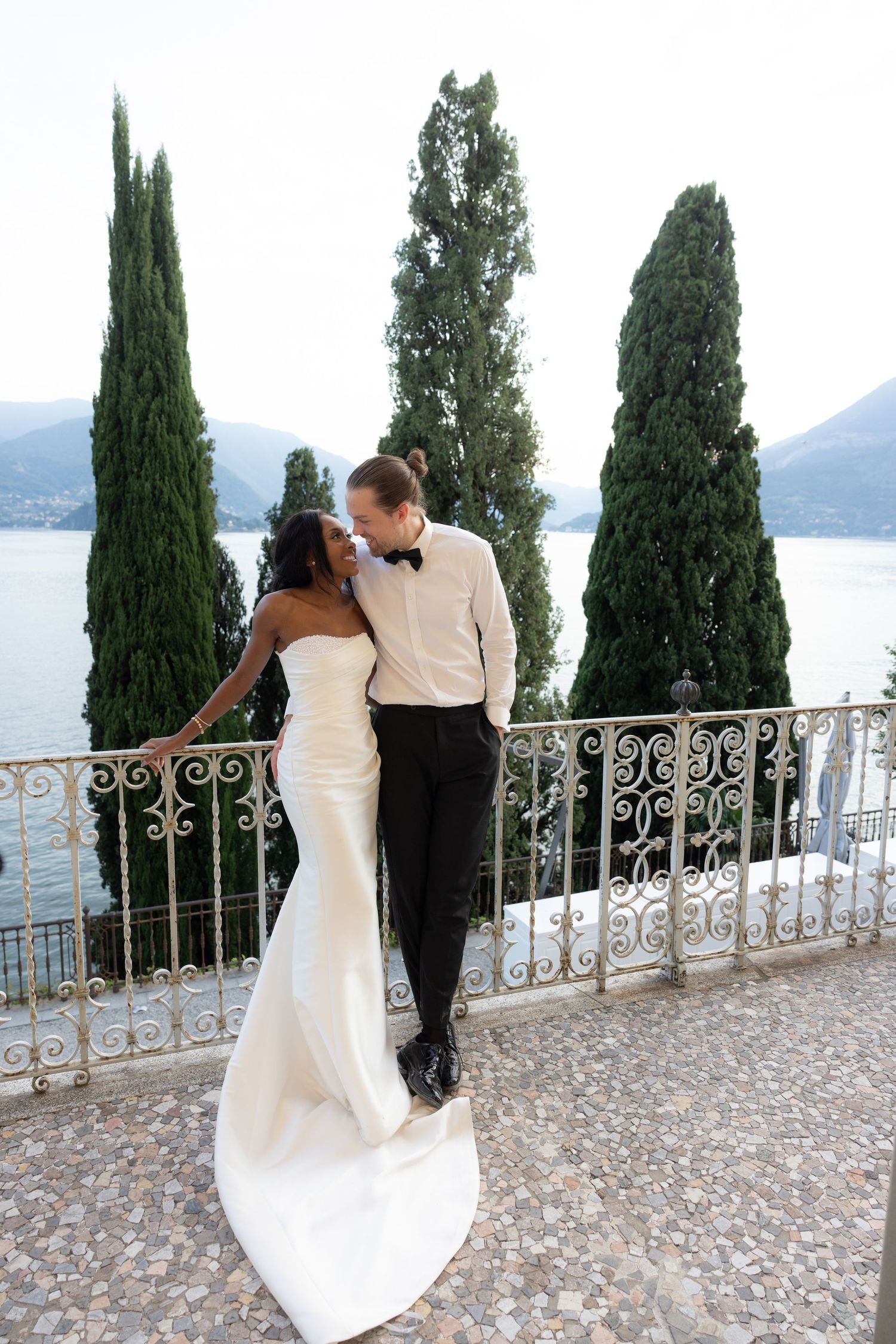 Romantic wedding couple shares intimate moments on a scenic terrace overlooking an Italian lake with cypress trees.