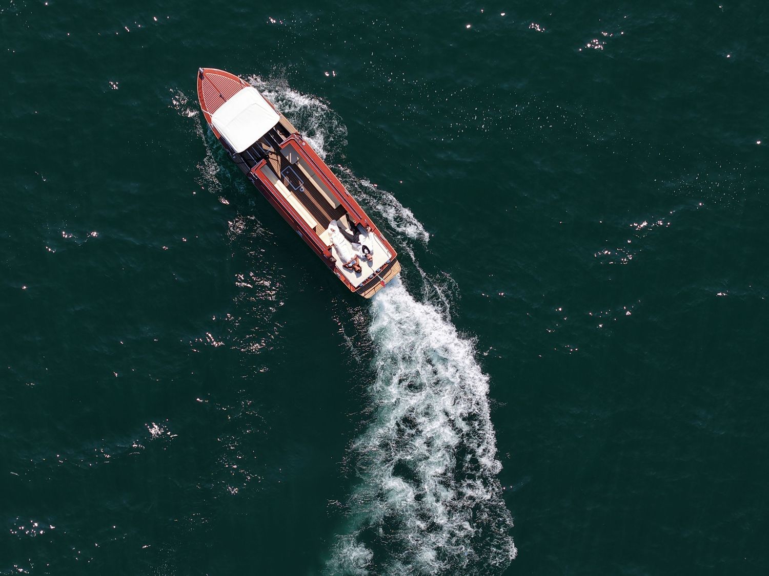 Wooden boat cutting through deep blue waters viewed from above.