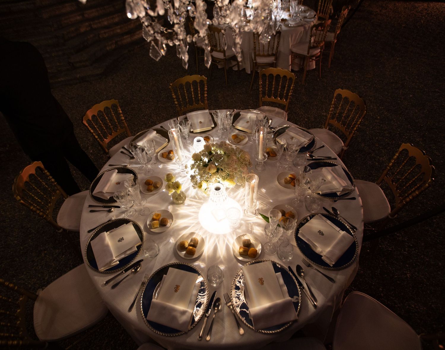 Intimate round dining tables with glowing chandelier centerpieces in dark reception setting.