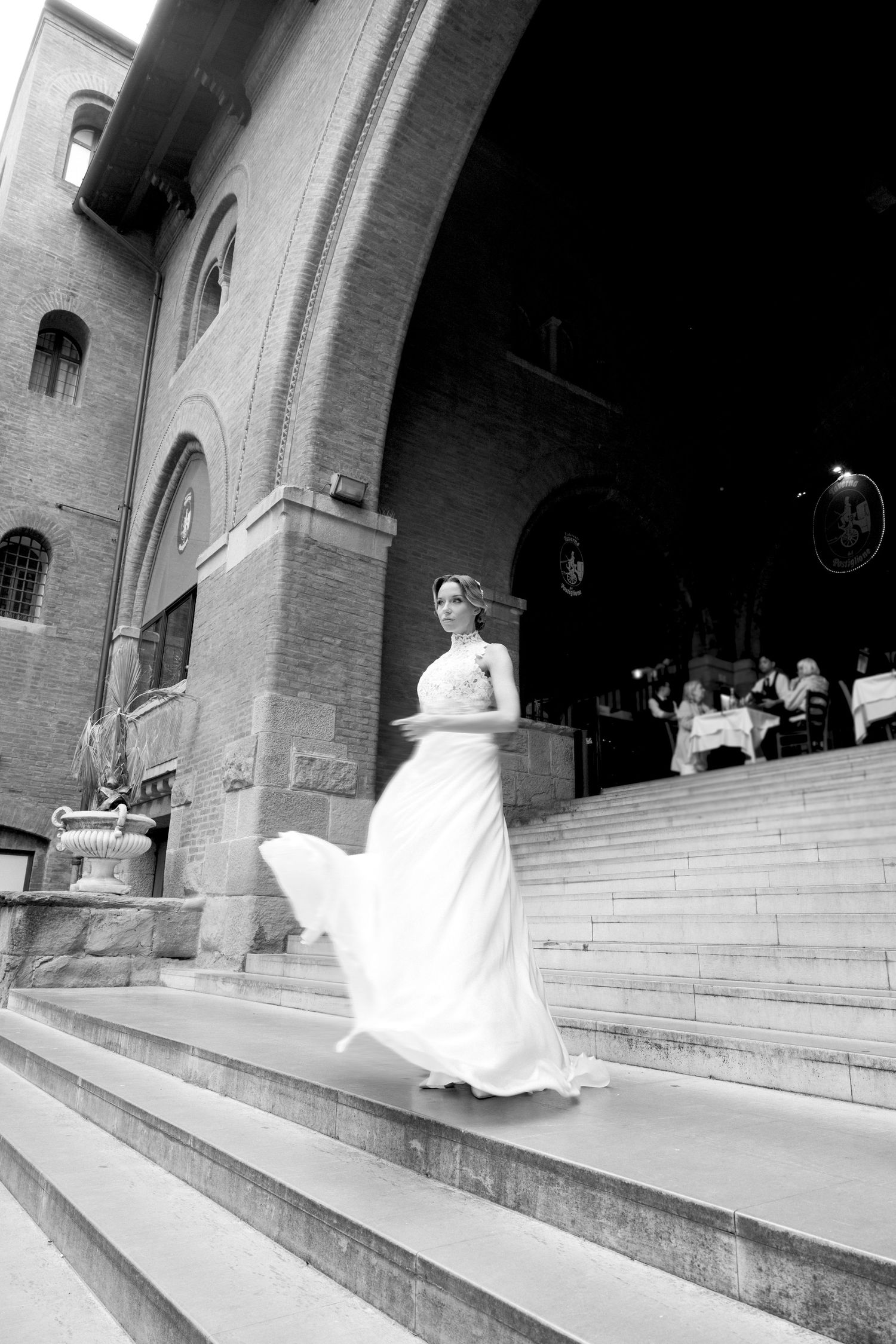 Wedding dress billowing dramatically on stone church steps in black and white photography.