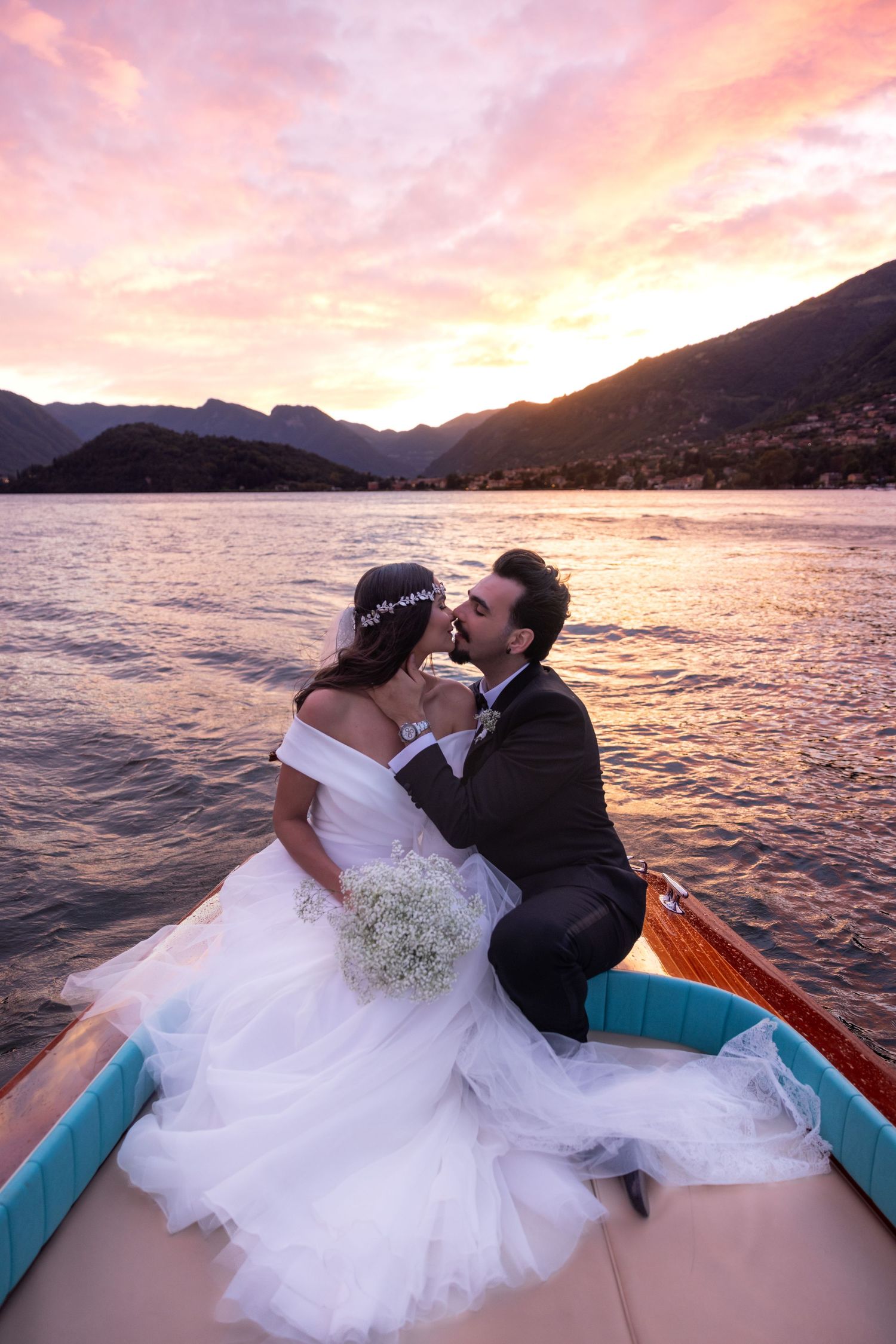 A romantic boat ride at sunset with mountains and lake creating a stunning backdrop for newlyweds.