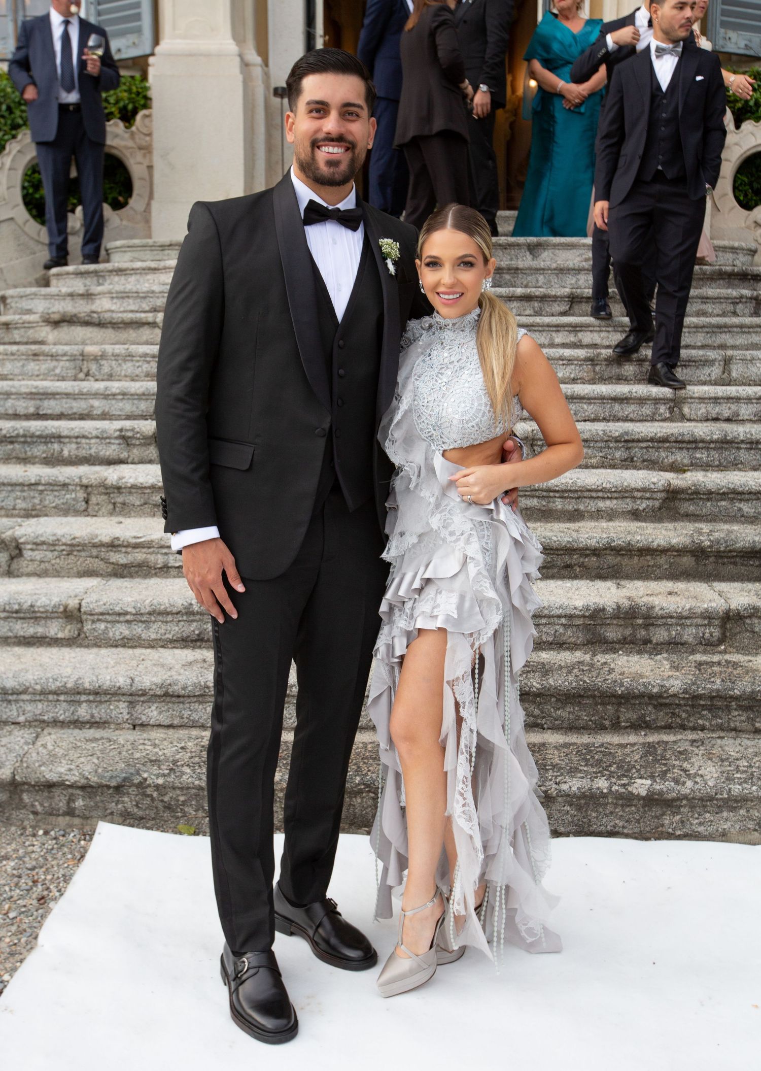 A couple poses on elegant stone steps with the groom in a black tuxedo and bride in a silver dress.