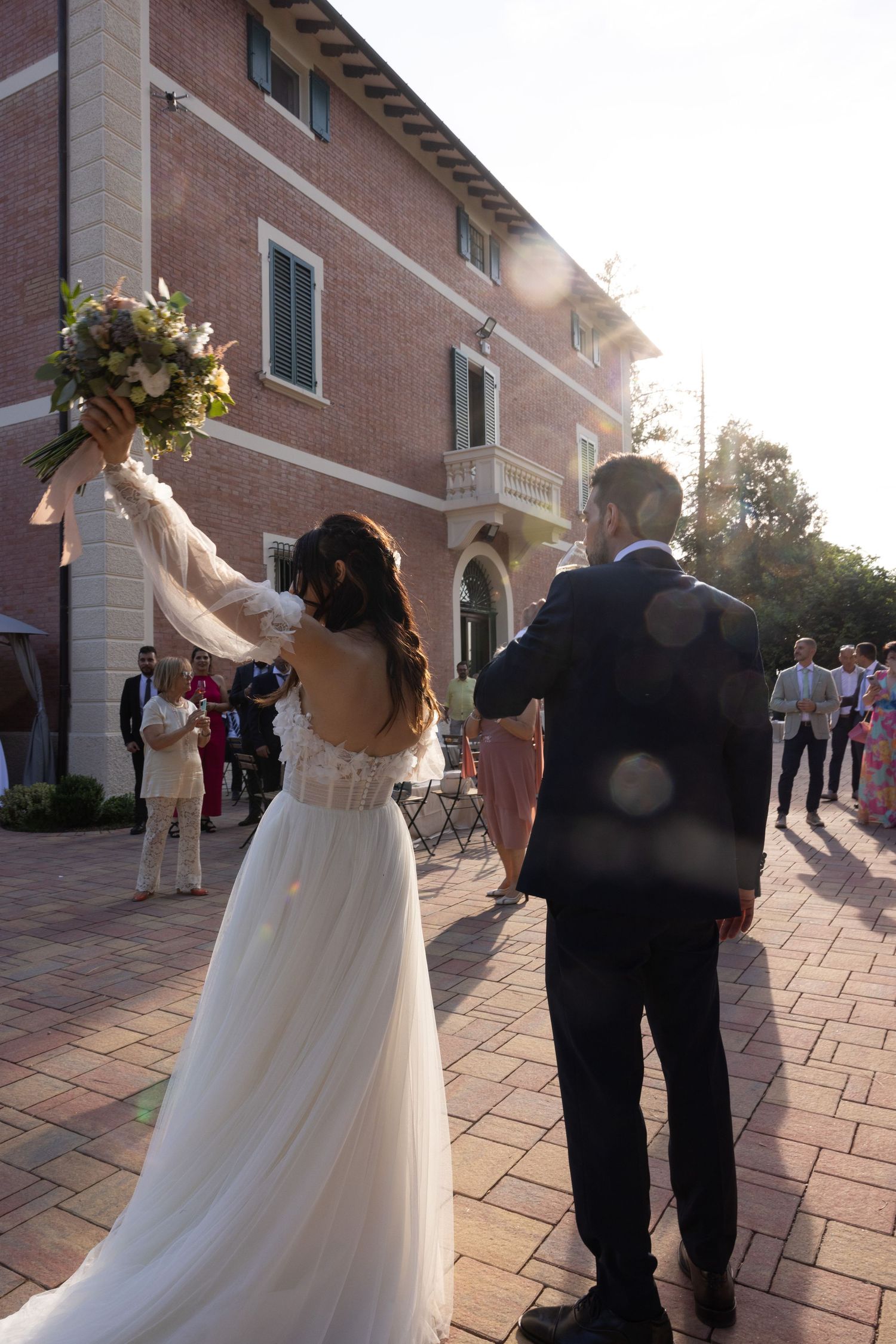 Wedding party dancing and celebrating on an outdoor brick patio at sunset.