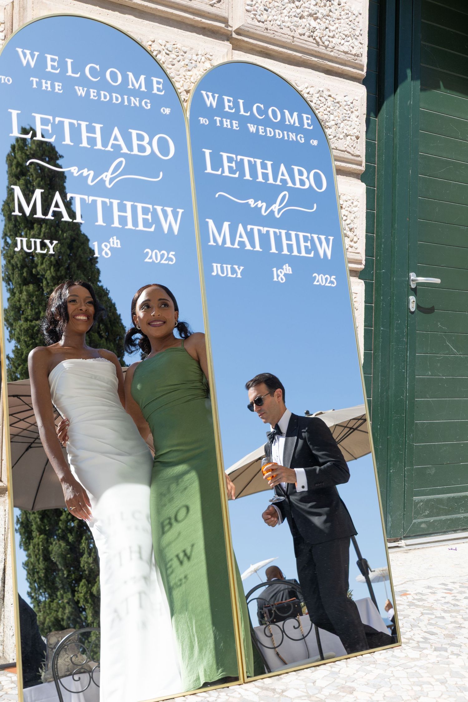 Wedding welcome sign in light blue displays text against white building exterior with green shutters.