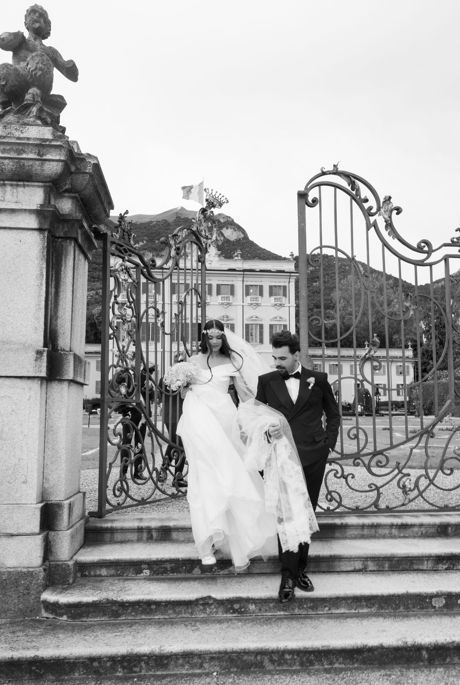 Vintage-style black and white wedding photos by ornate iron gates of grand estate.