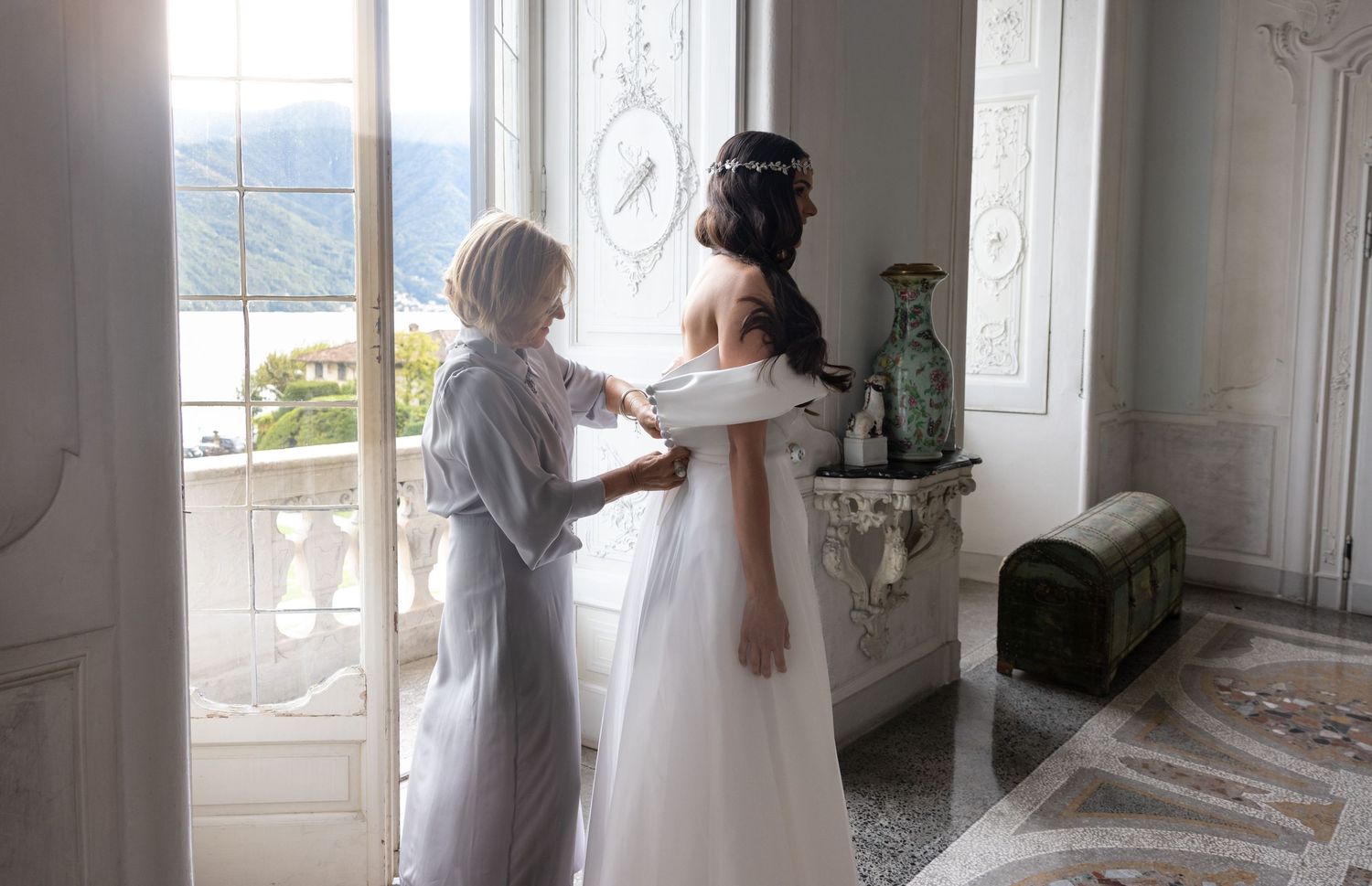 Wedding dress fitting in a bright sunlit room with elegant white decor.