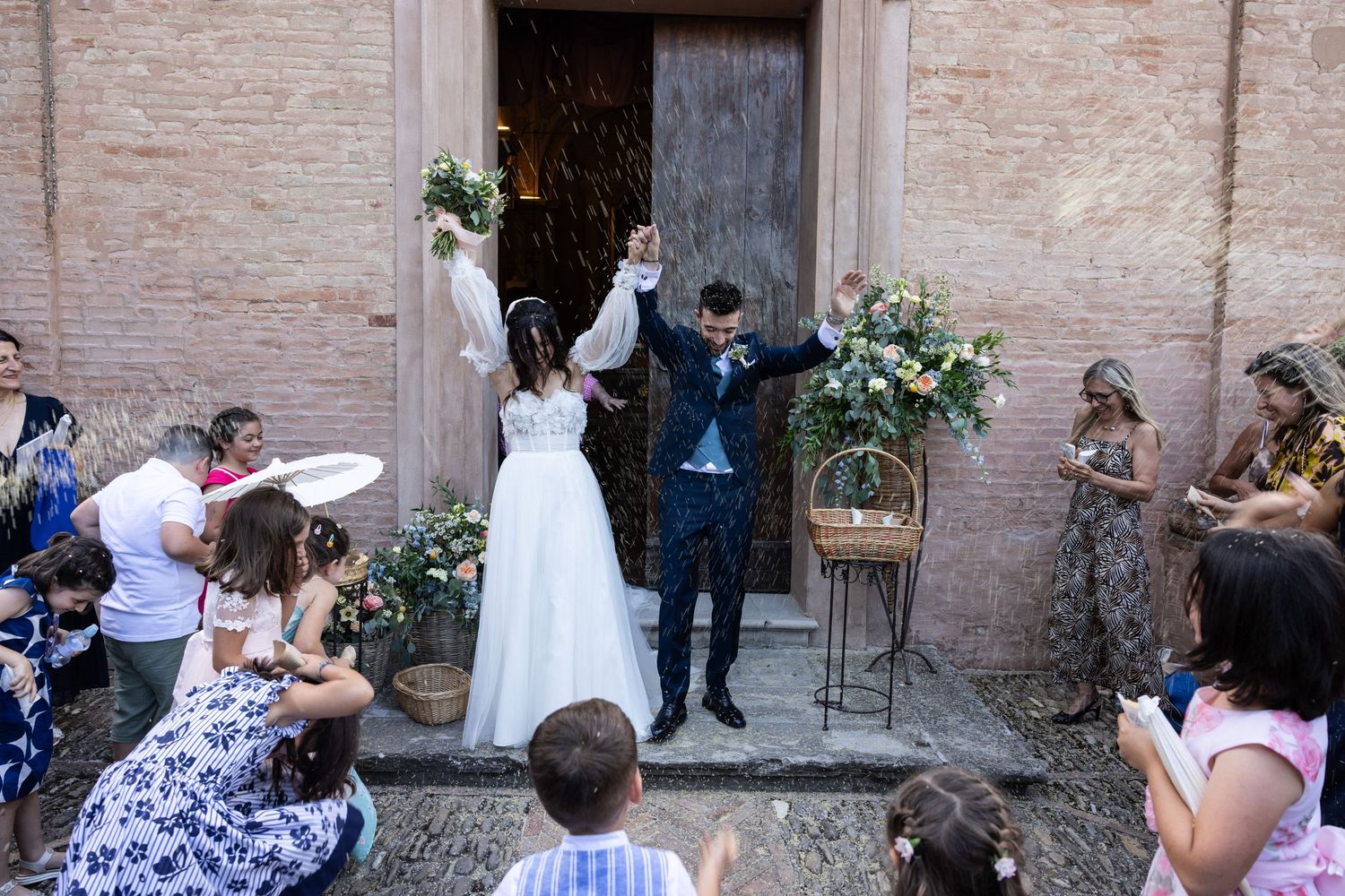 Guests mingle during an outdoor wedding reception against a rustic brick wall backdrop.