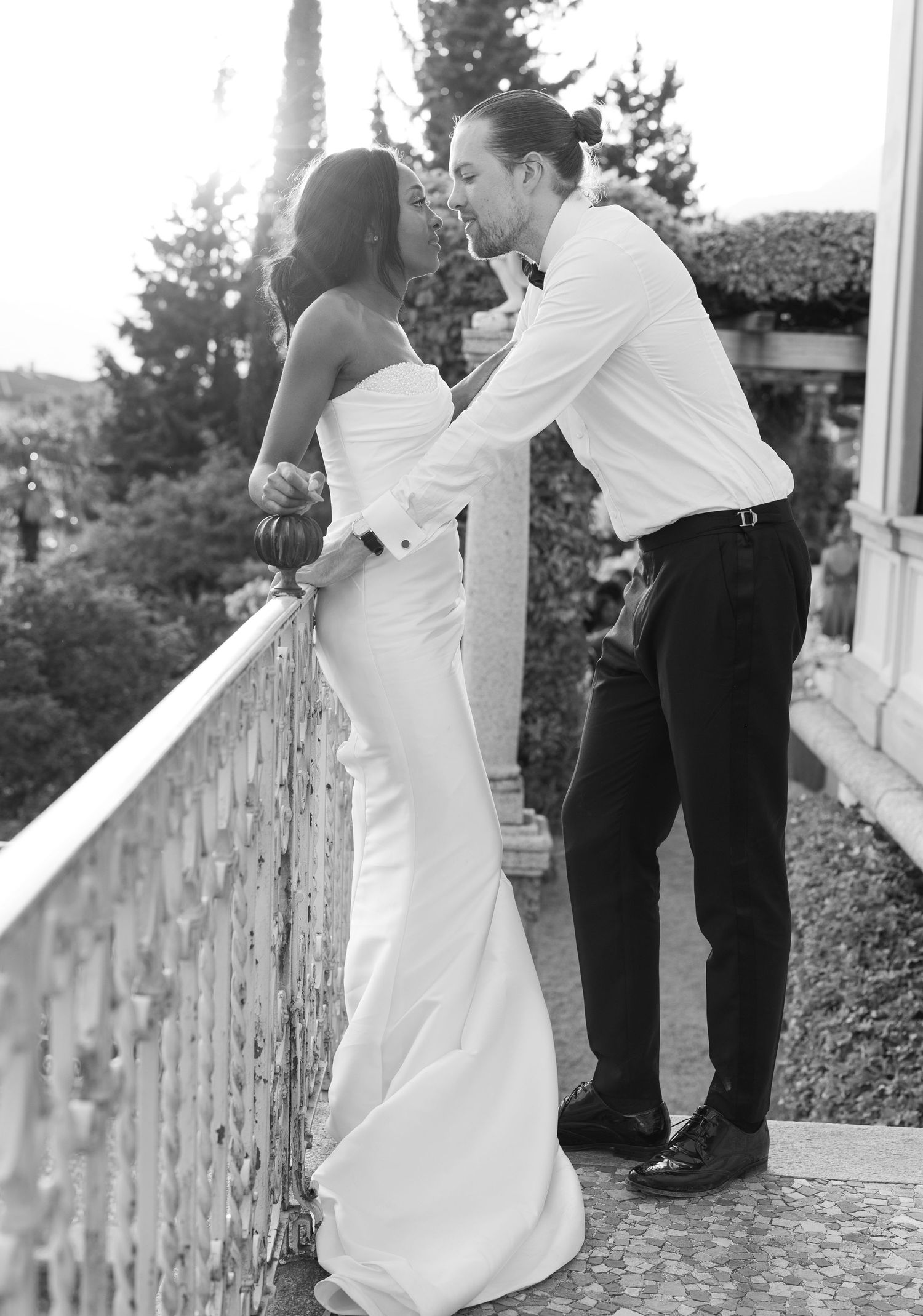 A romantic wedding couple dances together on a stone terrace surrounded by greenery in black and white.